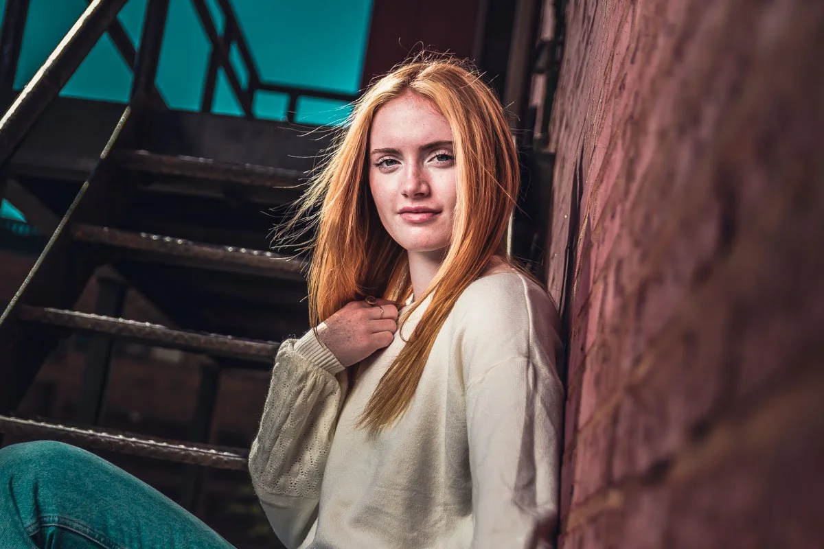 female senior leaning against brick wall on fire escape