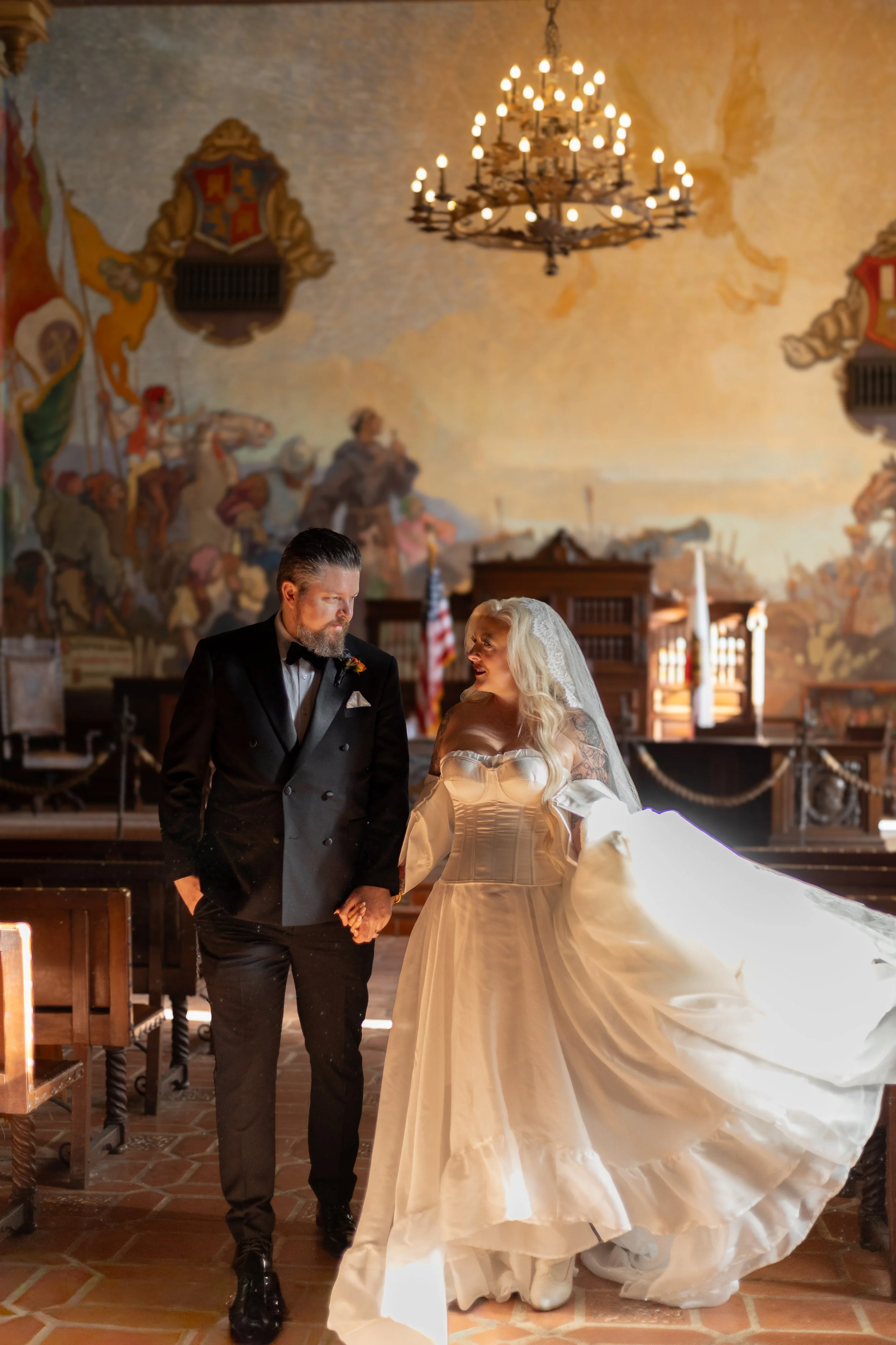 Bride and groom holding hands in Santa Barbara courthouse room ornately decorated with mural walls 