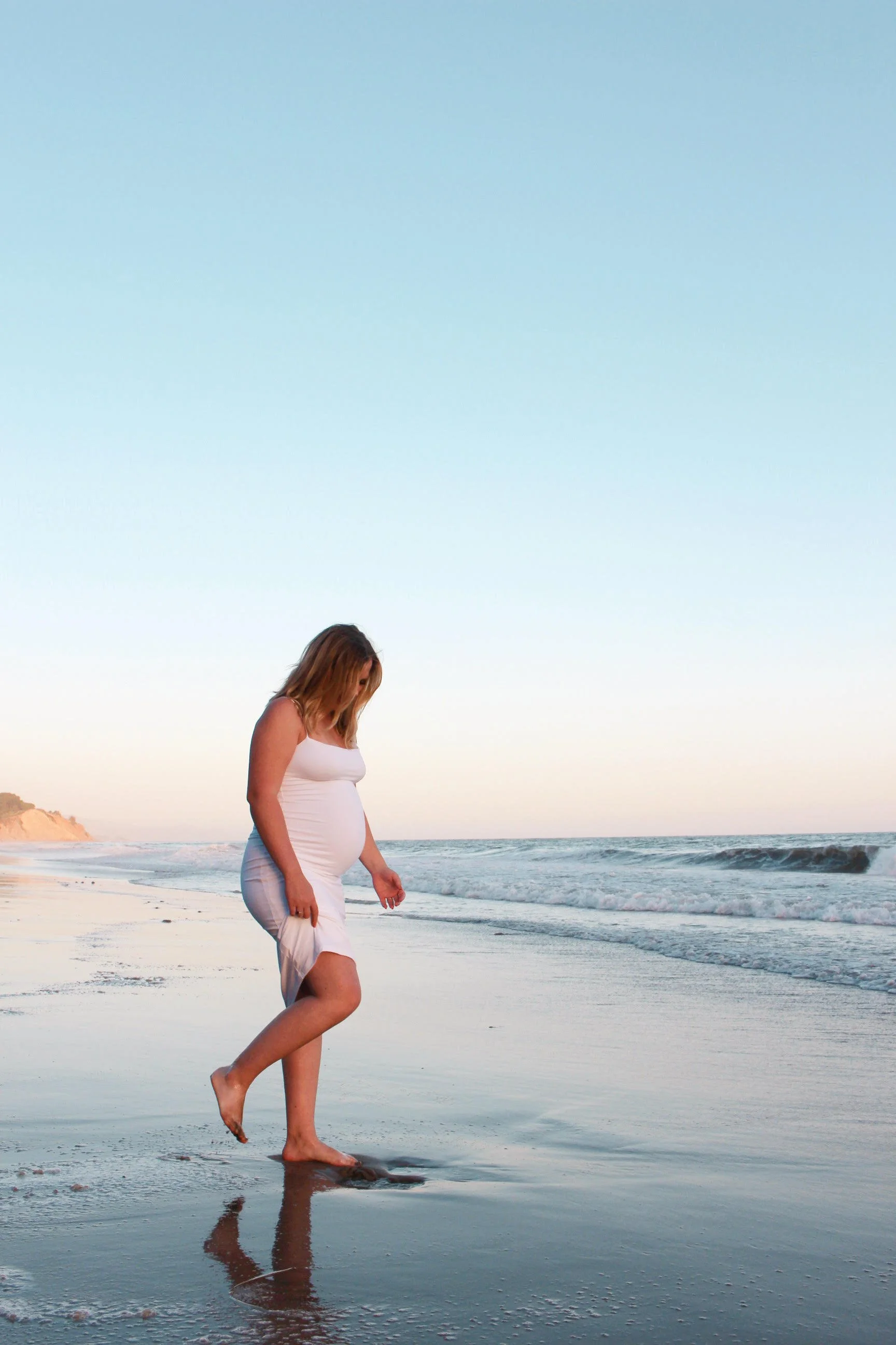 A pregnant woman walking barefoot on the sand for a maternity photoshoot in Santa Barbara, CA