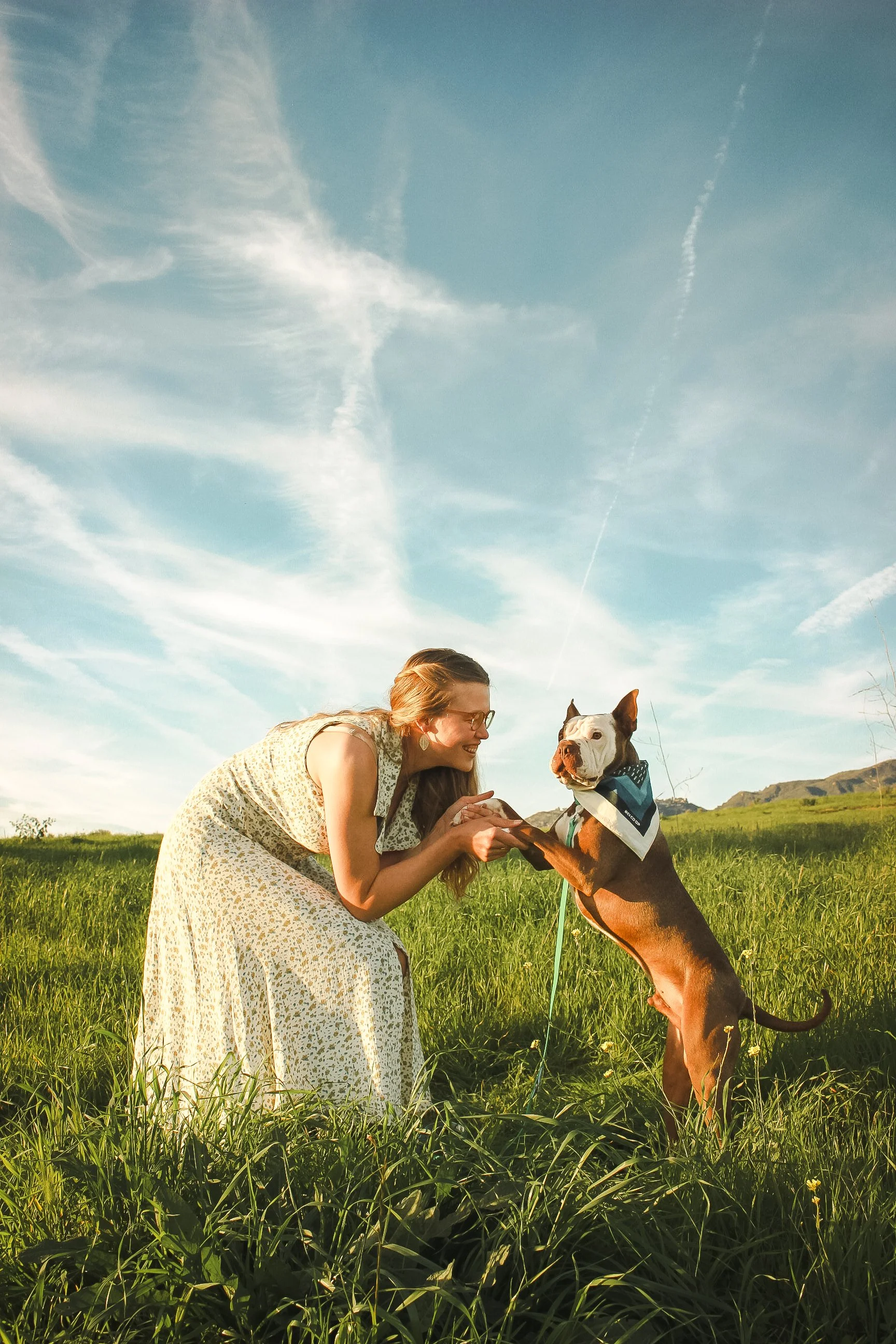 A woman in a floral dress playing with a dog in a grassy field during the daytime in Santa Barbara