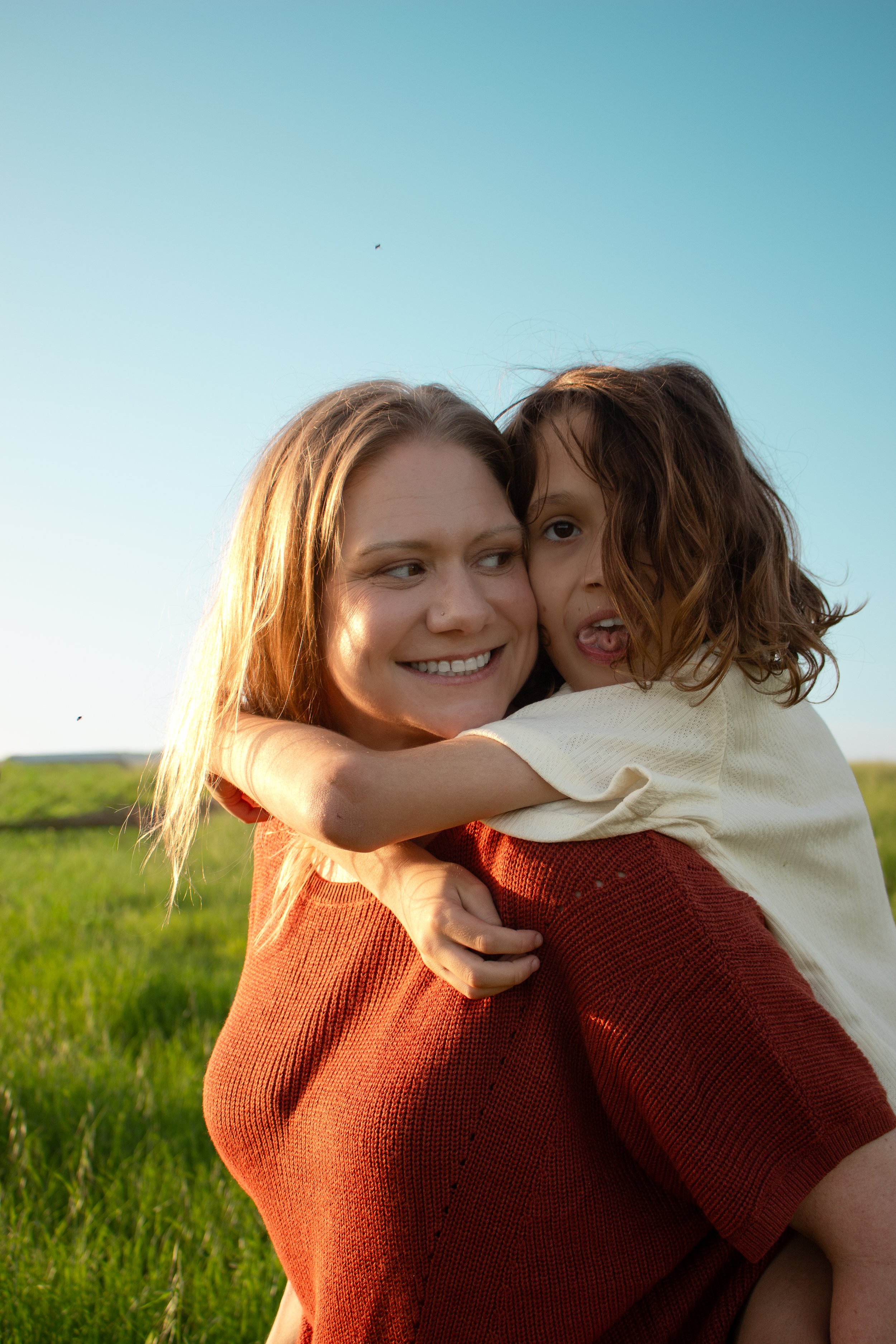 A woman smiling as she holds her child on her back in a grassy field for a photoshoot in Santa Barbara