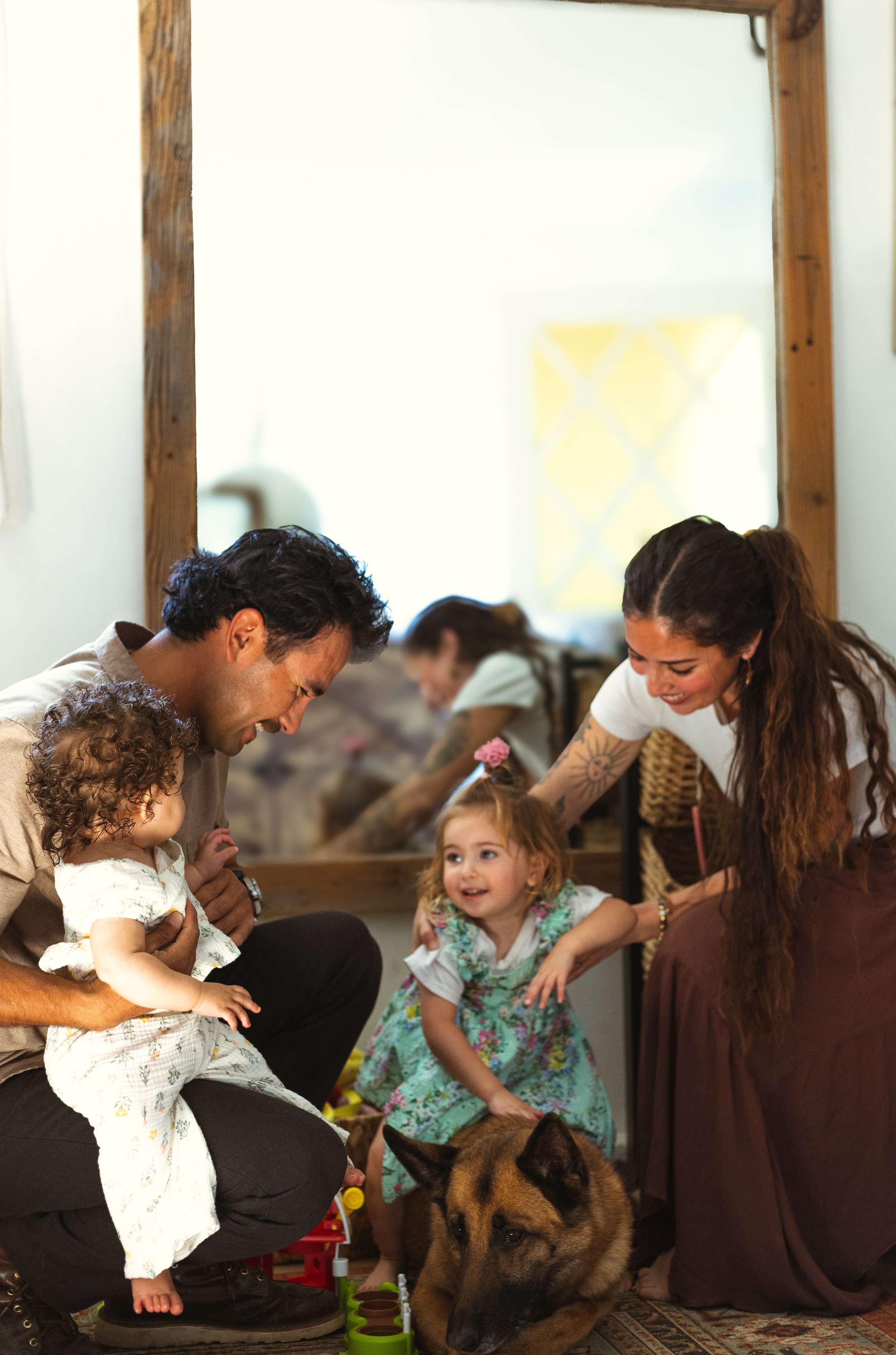 A family with two young children and a dog, enjoying a joyful moment indoors with a mirror reflecting the scene.