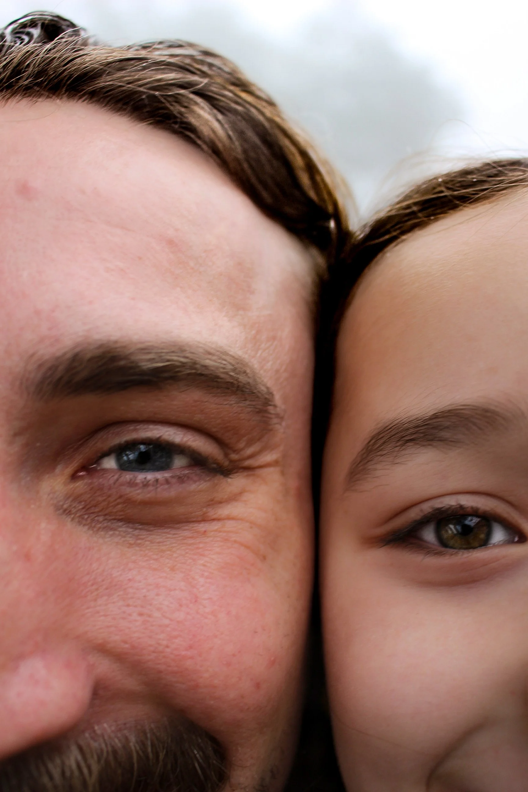 Close-up of a man and his daufhter with their faces pressed together, both smiling and looking at the camera.