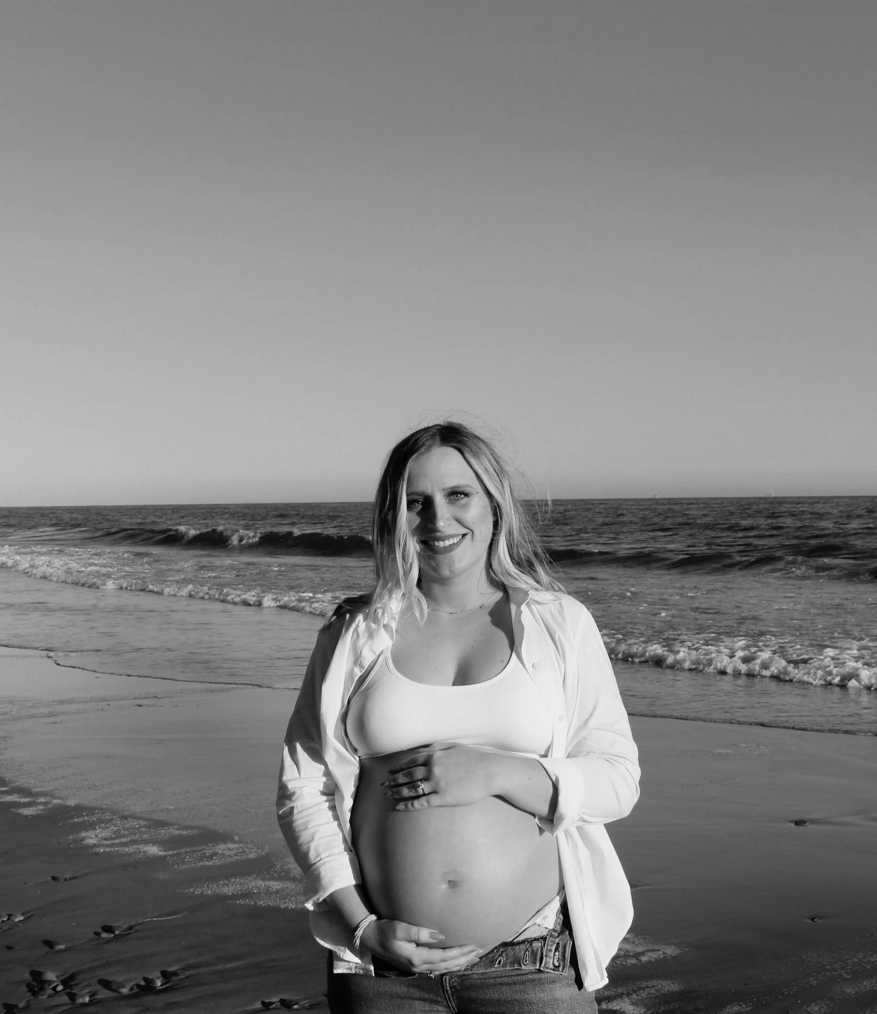 A pregnant woman smiling at the beach in Montecito for a maternity photo shoot 