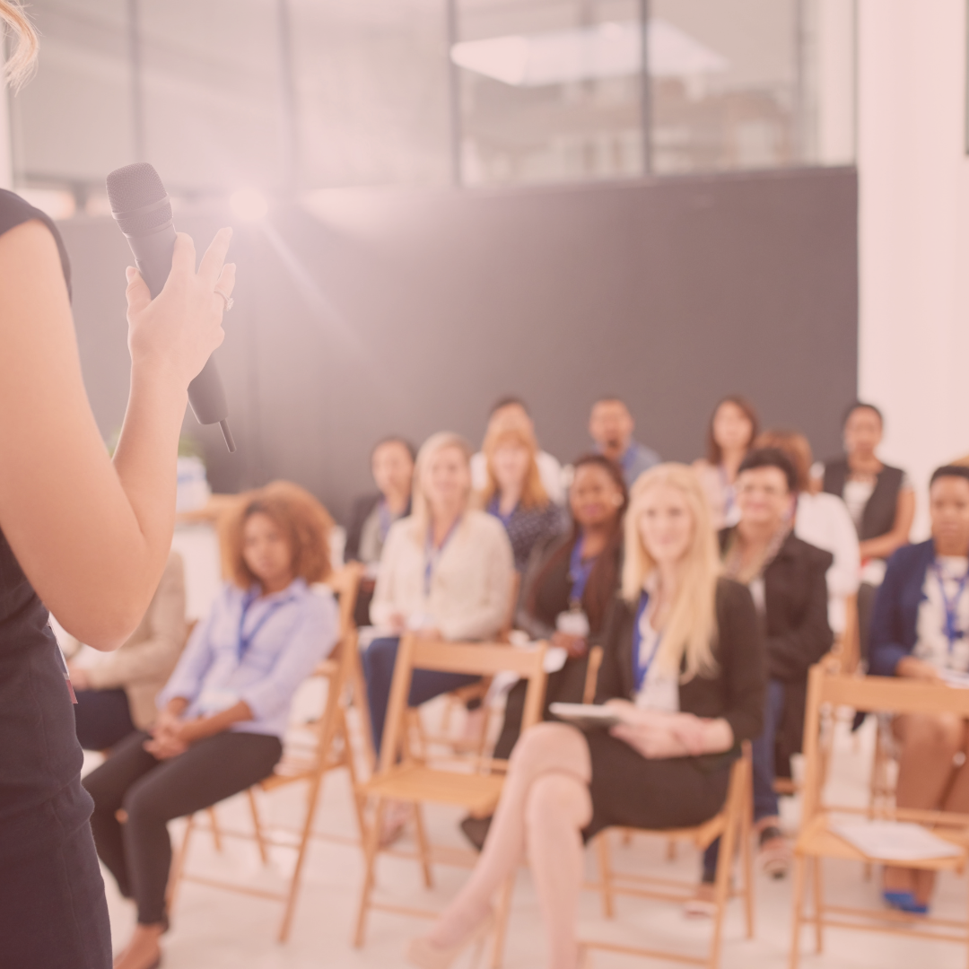 Women with a microphone speaking to a crowd at a conference