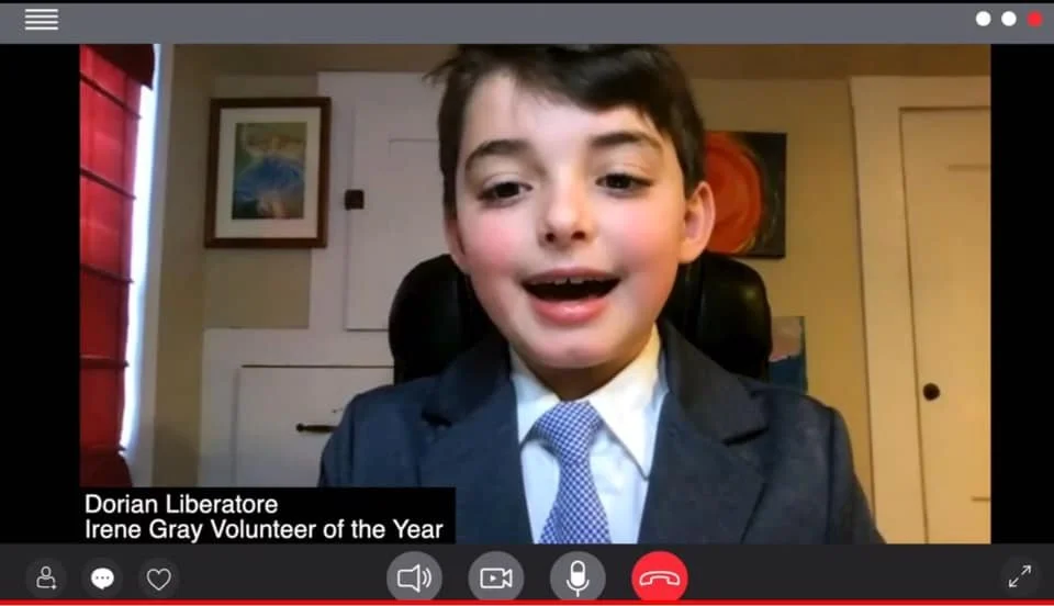 Young boy dressed in a suit and tie, participating in a video call or virtual event.