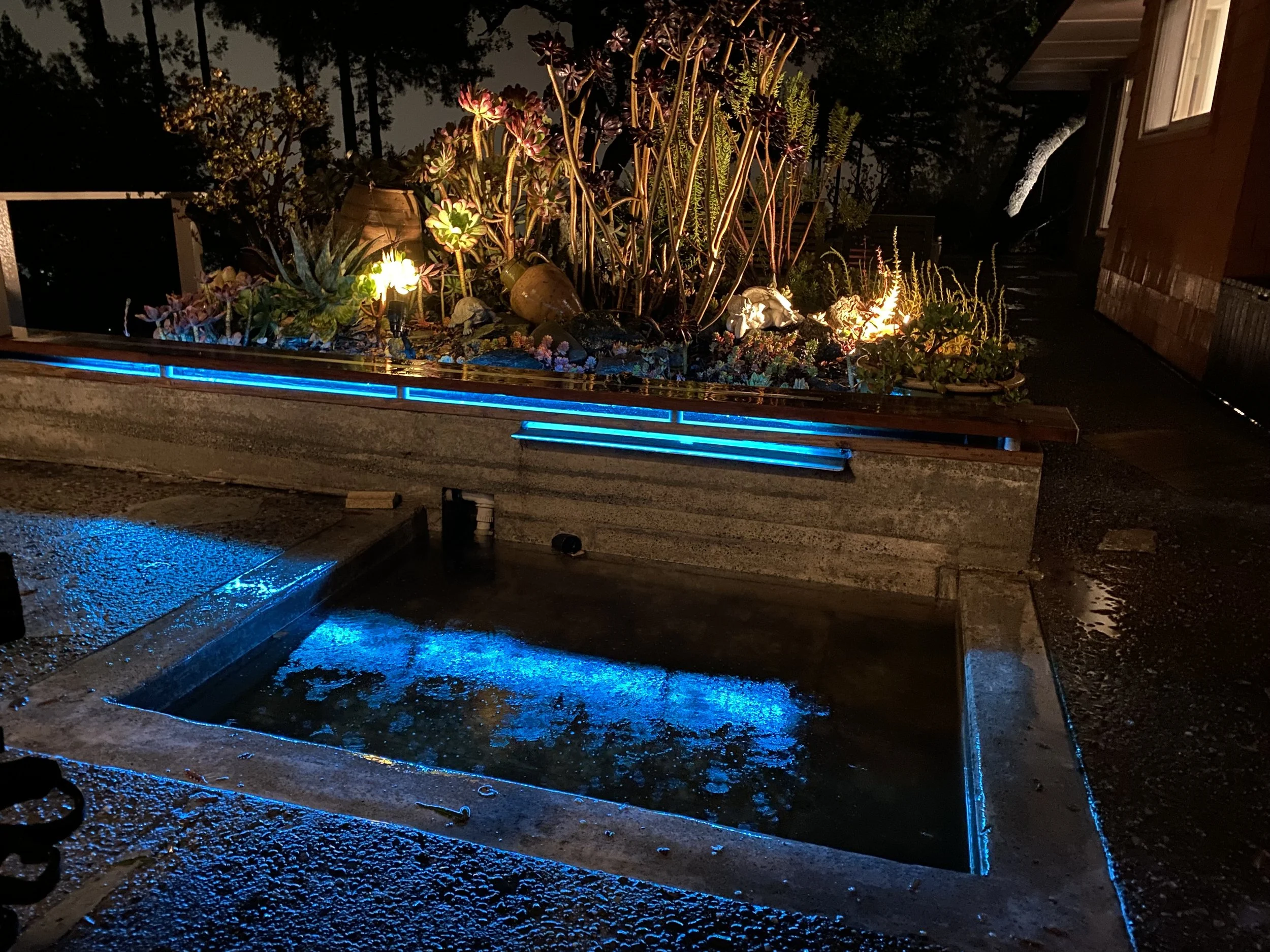 Outdoor concrete fountain with LED and water flume, redwood bench on top held by aluminum cylinders