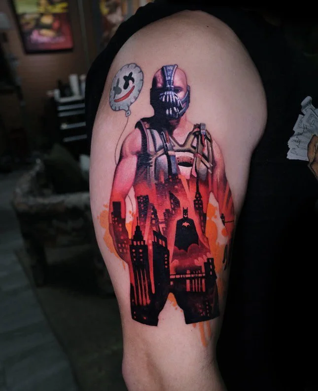 Tattoo of a muscular man wearing a mask and tactical gear with a city skyline silhouette and Batman symbol on the thigh, and a floating speech bubble with a distressed smiley face.