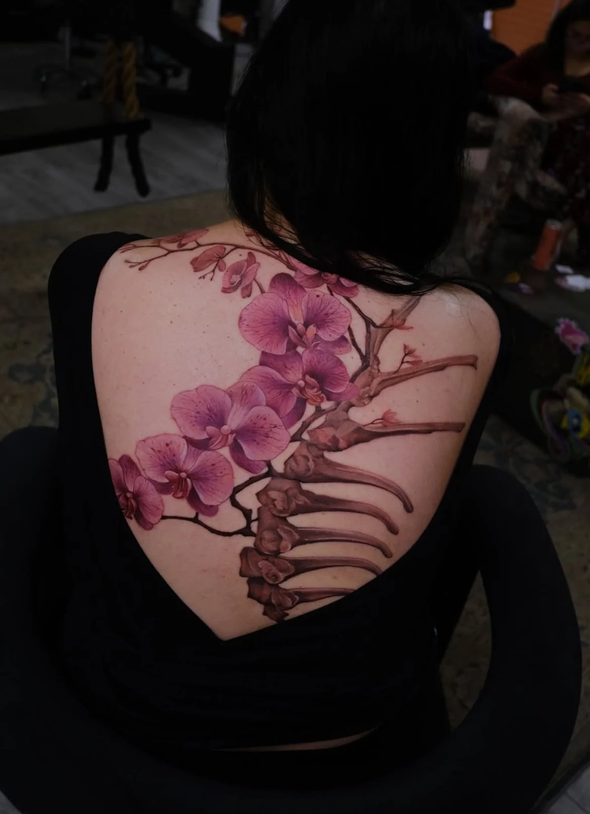 Back tattoo of pink orchid flowers and a stylized illustration of a spine on person's back.