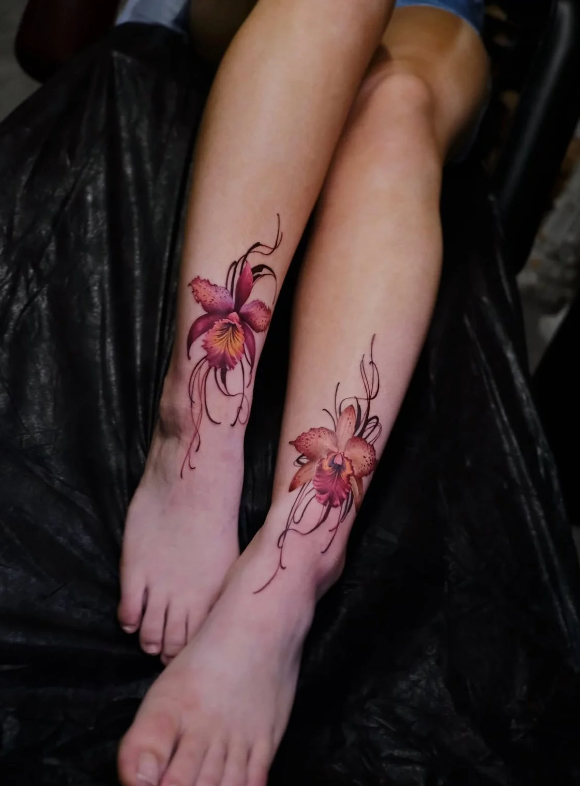 Two legs with matching pink and orange orchid tattoos on the calves.