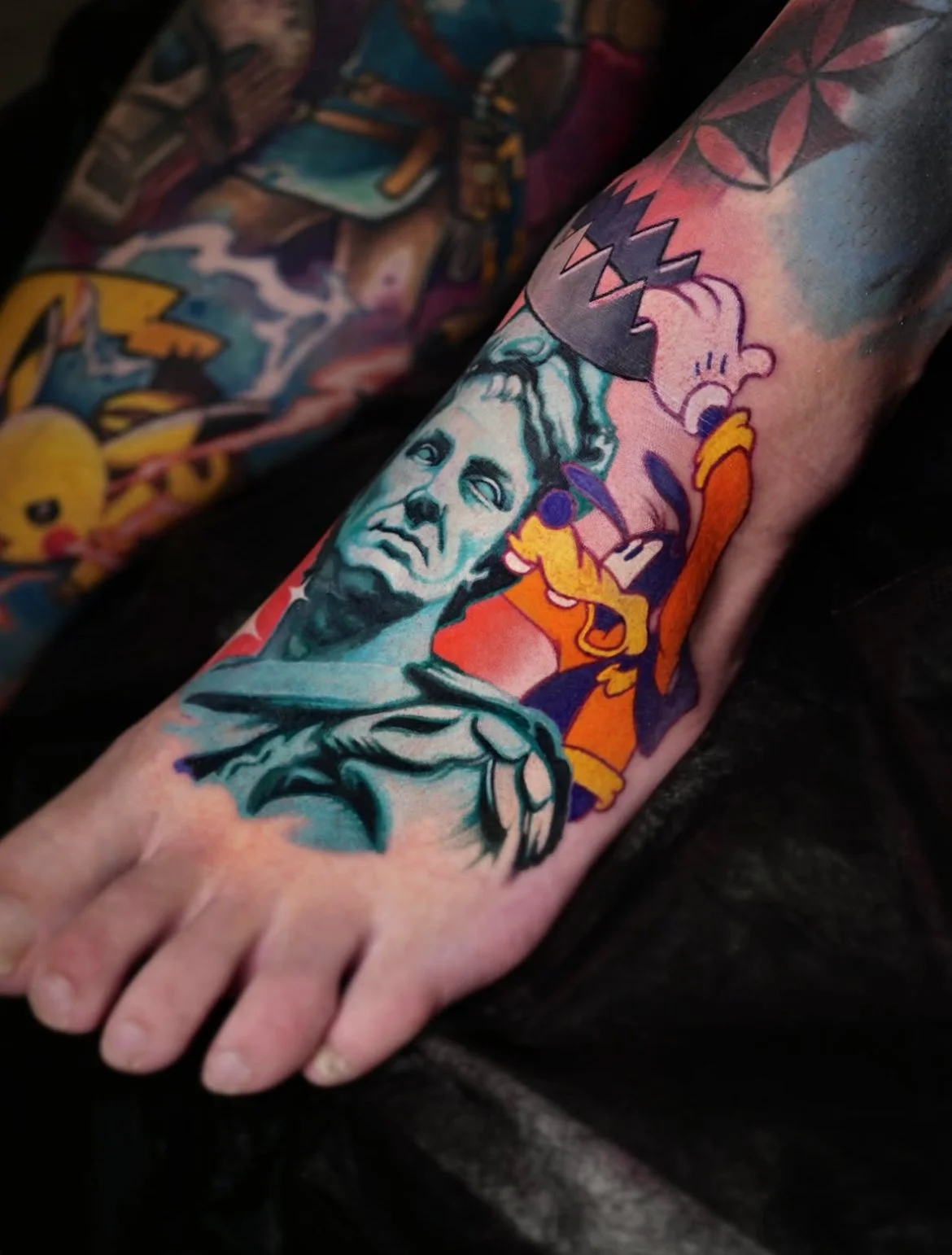 Colorful tattoo on forearm featuring a portrait of a man, Mickey Mouse, and a cartoonish creature biting into a zipper.