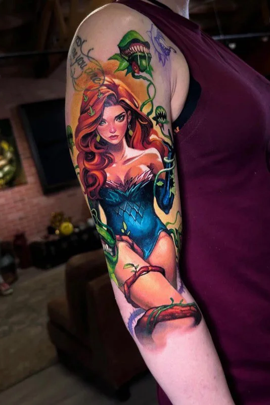 A tattoo of a female character with long, wavy brown hair and a blue dress, surrounded by green vines and snake-like elements, on a person's upper arm.