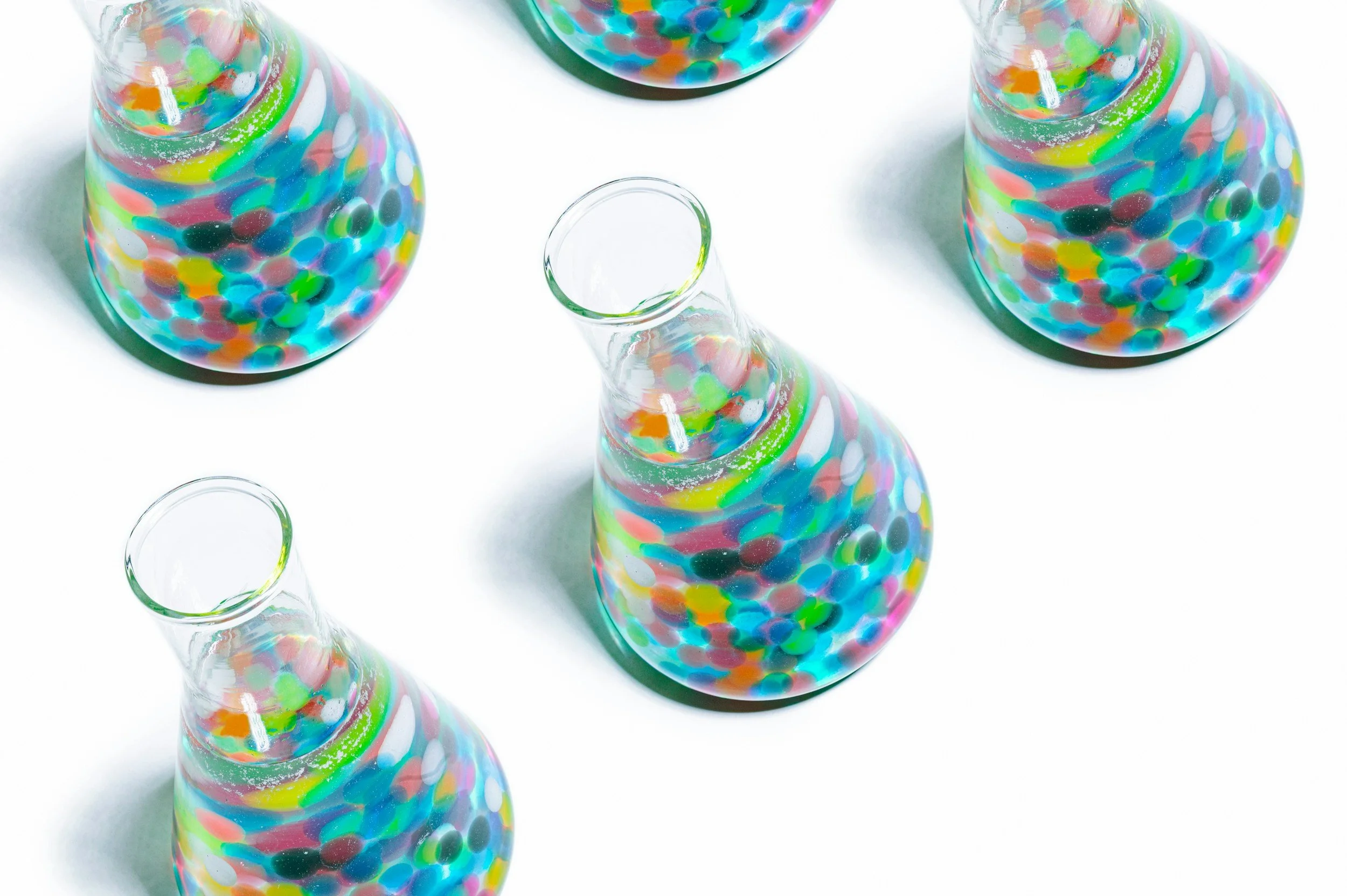 Four glass vases filled with colorful, round confetti-like objects on a white background.