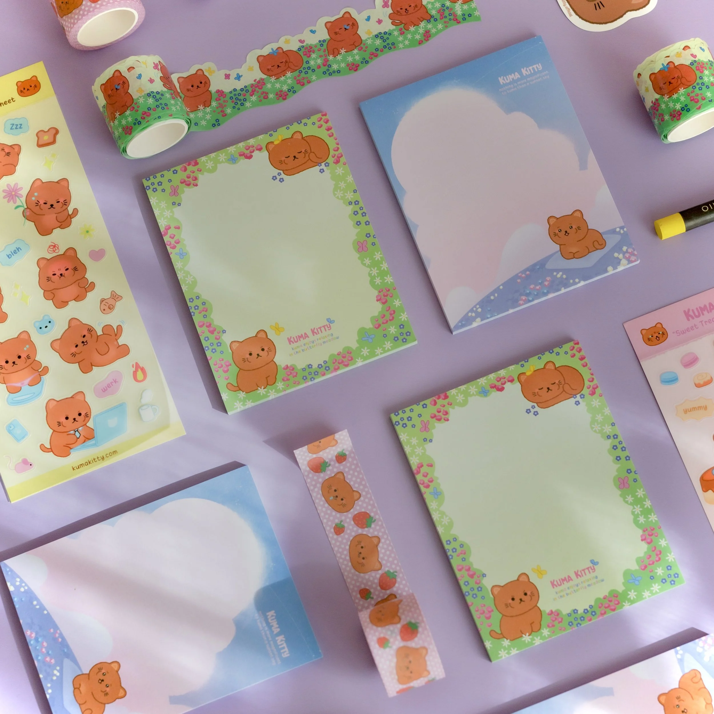 Various Kumamon-themed stationery items including notebooks, stickers, washi tape, and page markers featuring cute bear characters in bright colors on a purple background.