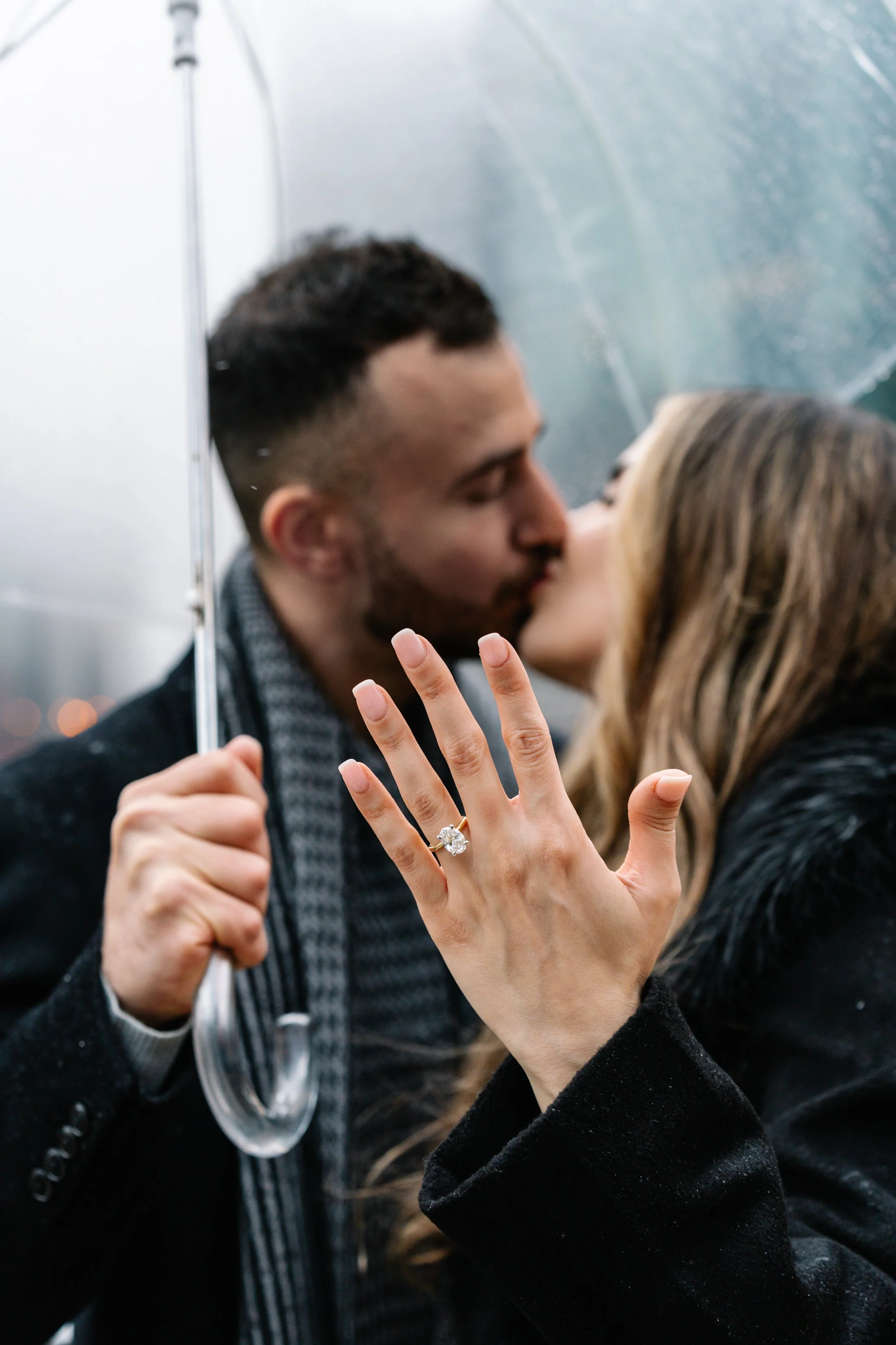 A couple kissing under an umbrella, with the woman's hand showing an engagement ring.