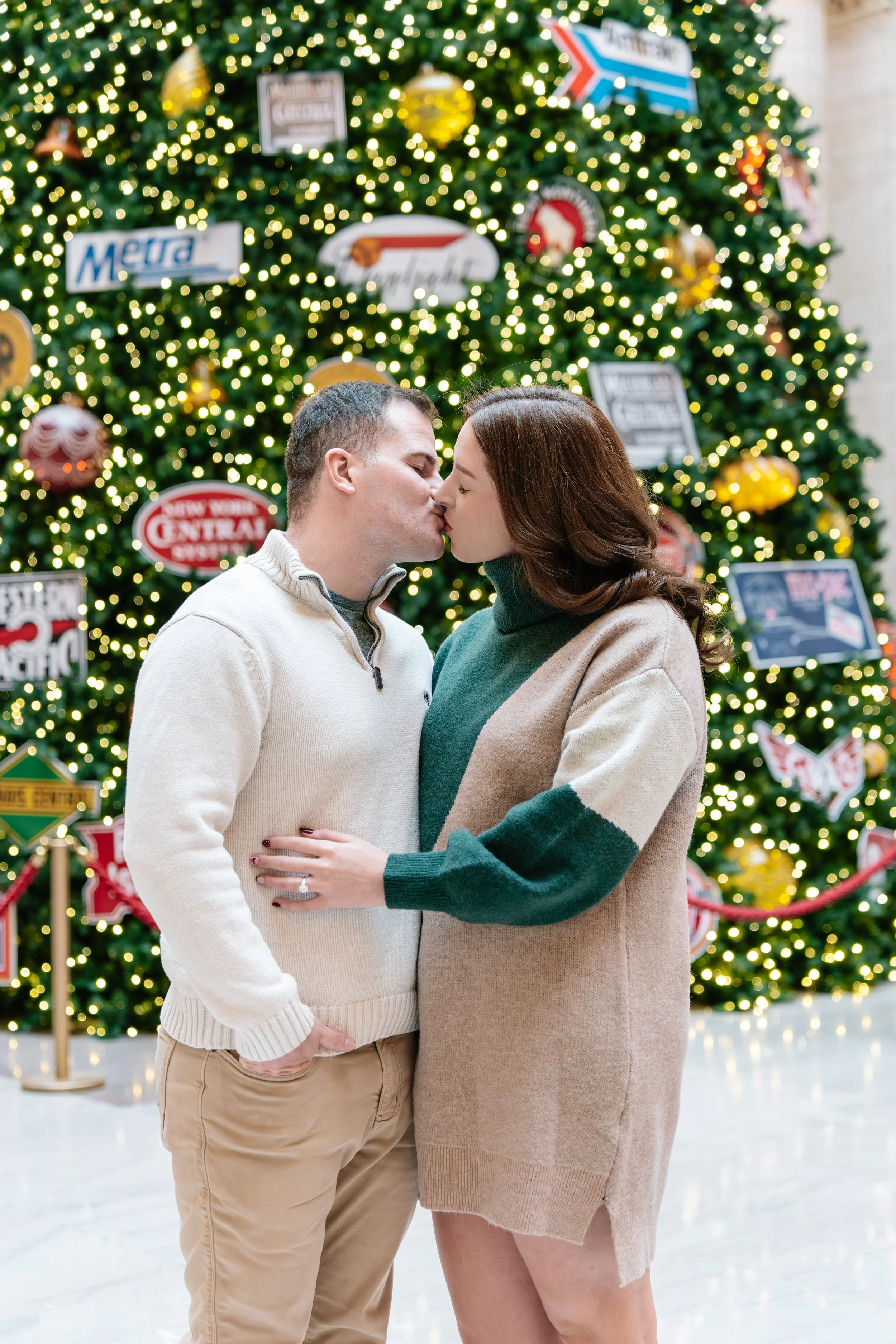 A couple sharing a kiss in front of a decorated Christmas tree.