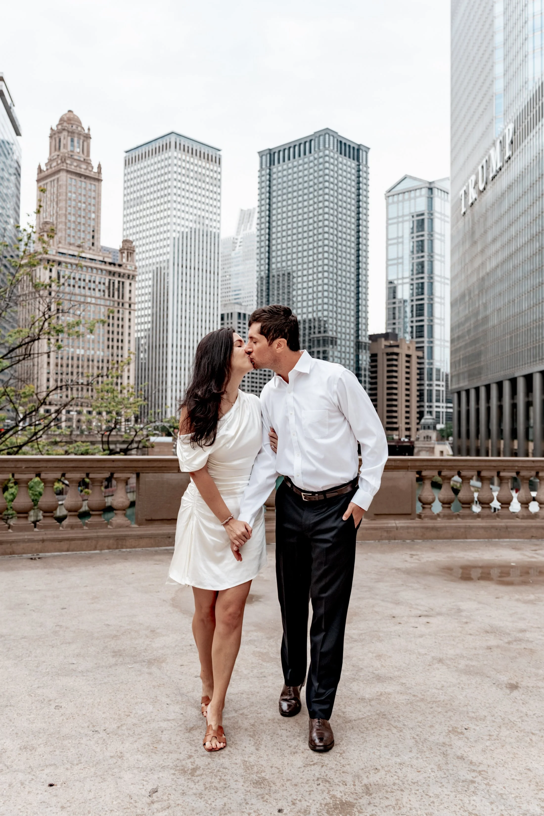 A couple is kissing on a balcony in front of a cityscape with tall skyscrapers.