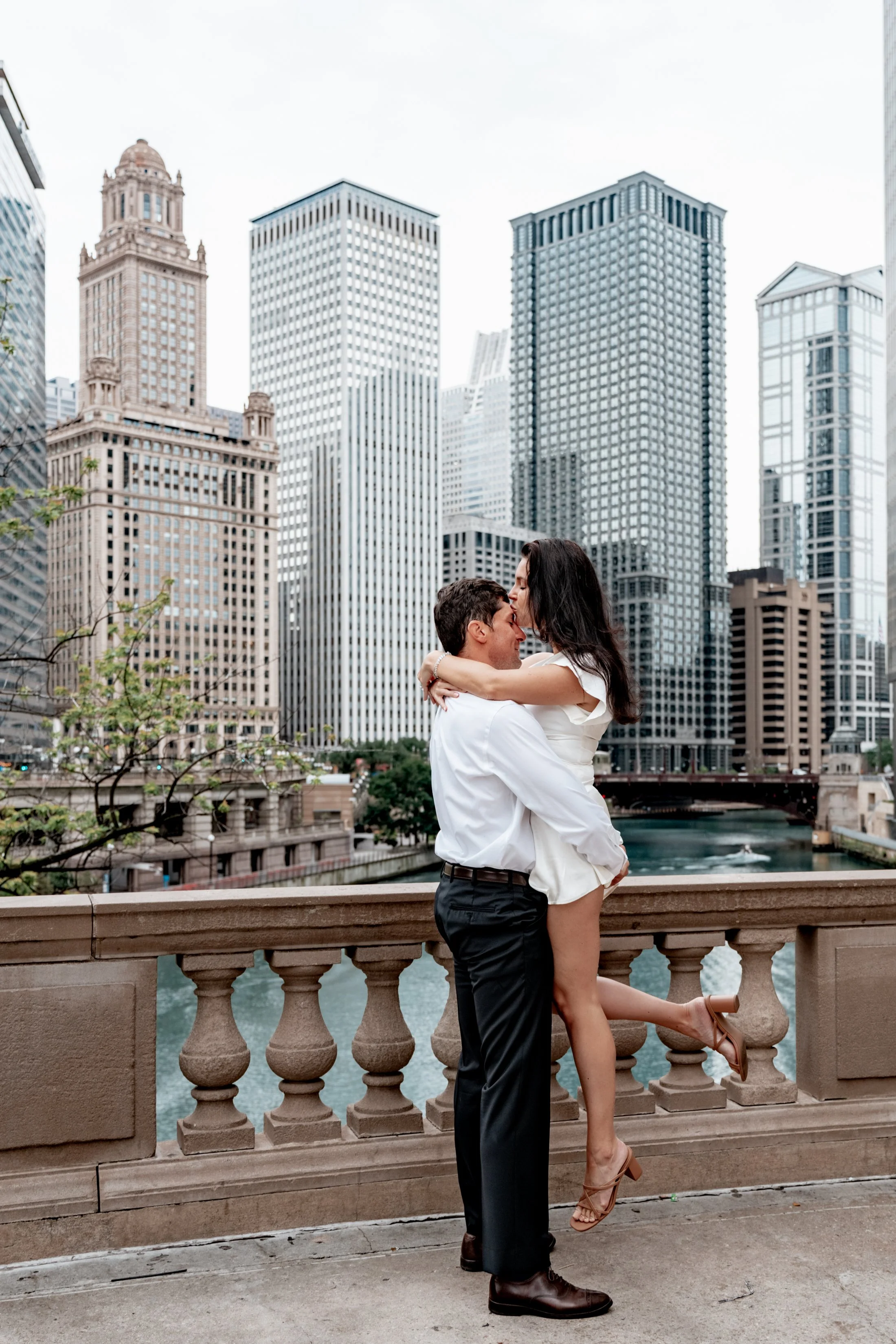 A couple kissing on a bridge with a city skyline in the background.