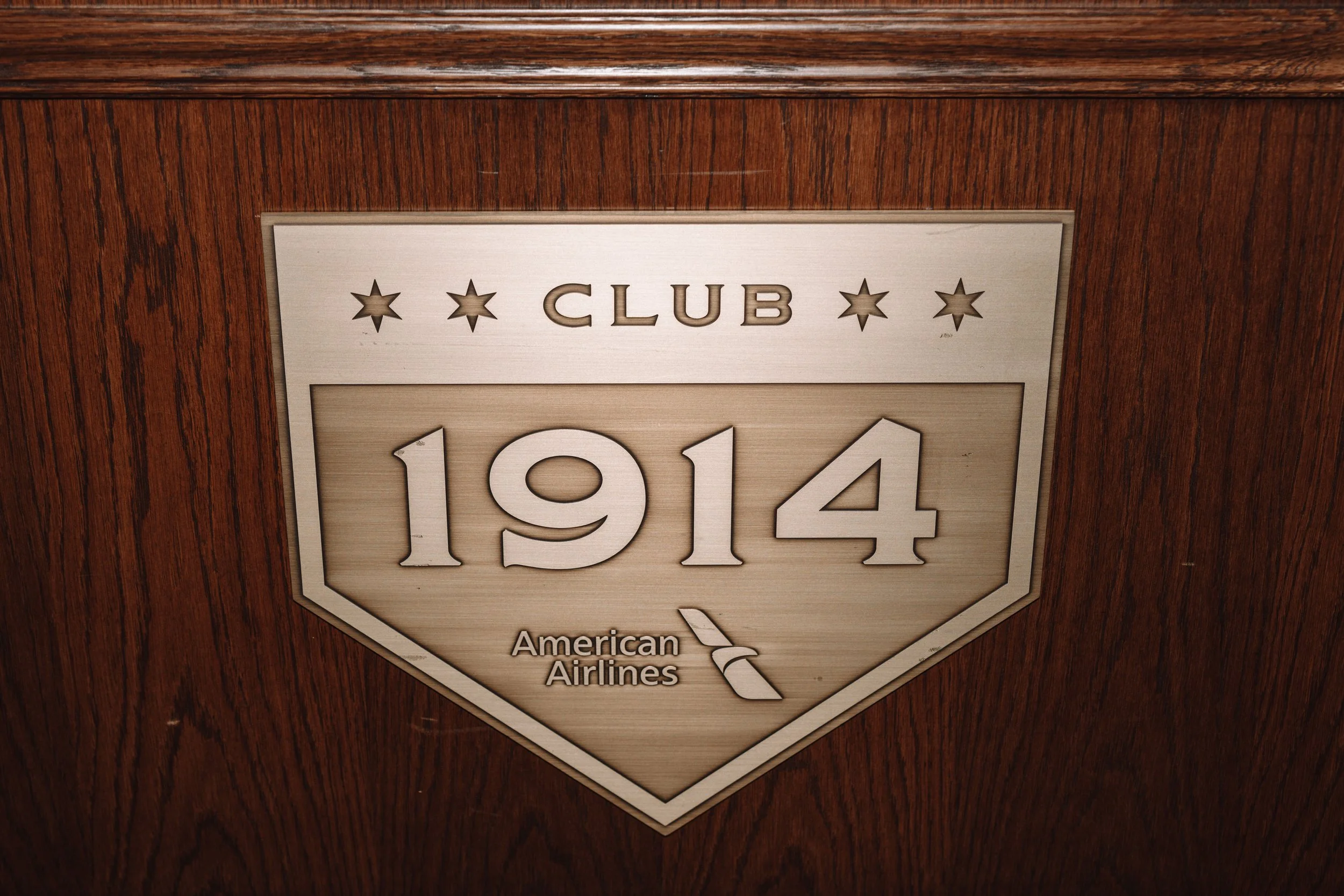 A wooden plaque with a metallic emblem that reads 'Club 1914', featuring four stars above the text and the American Airlines logo below.