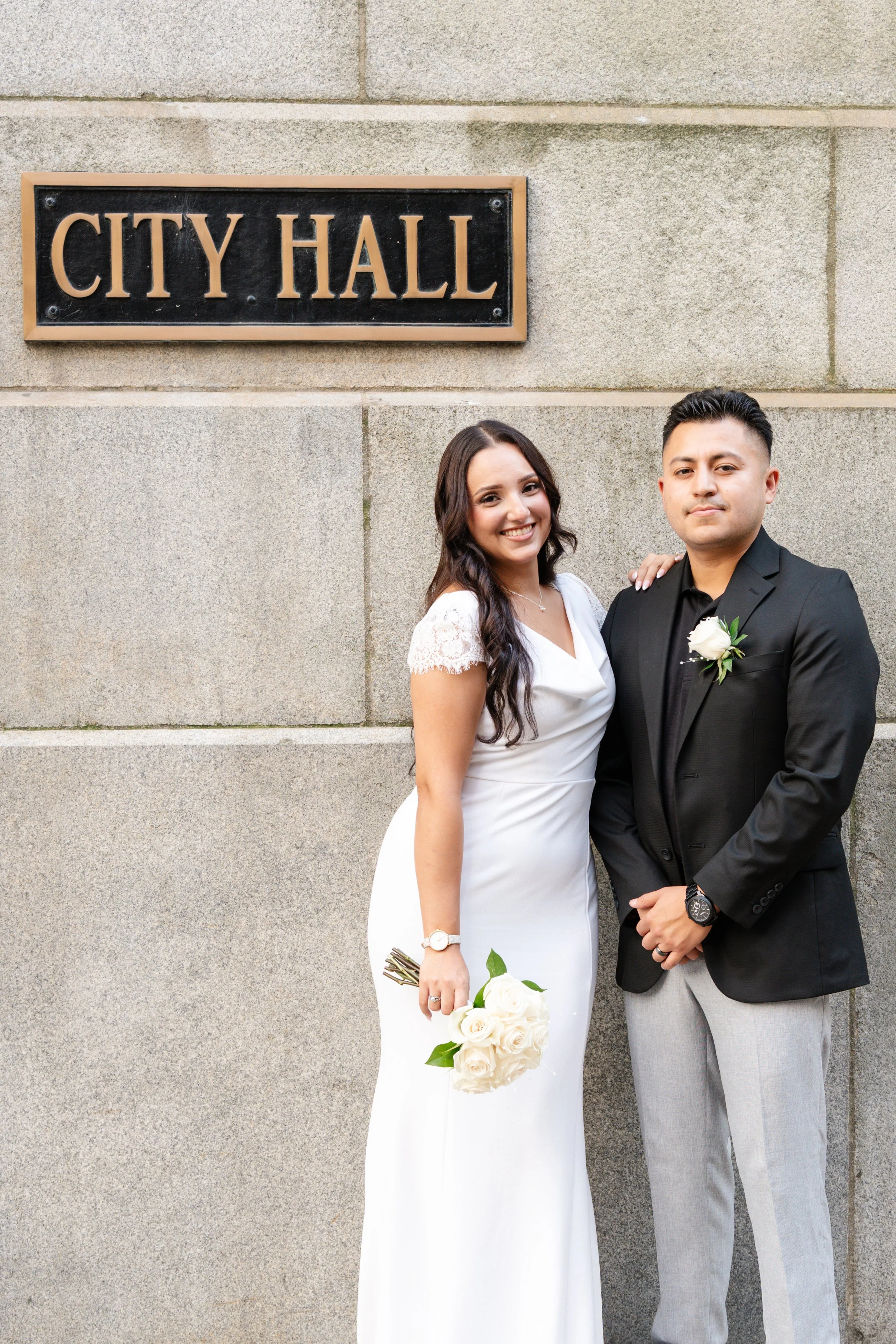 A happy bride and groom standing outside a city hall building, posing for a photo.