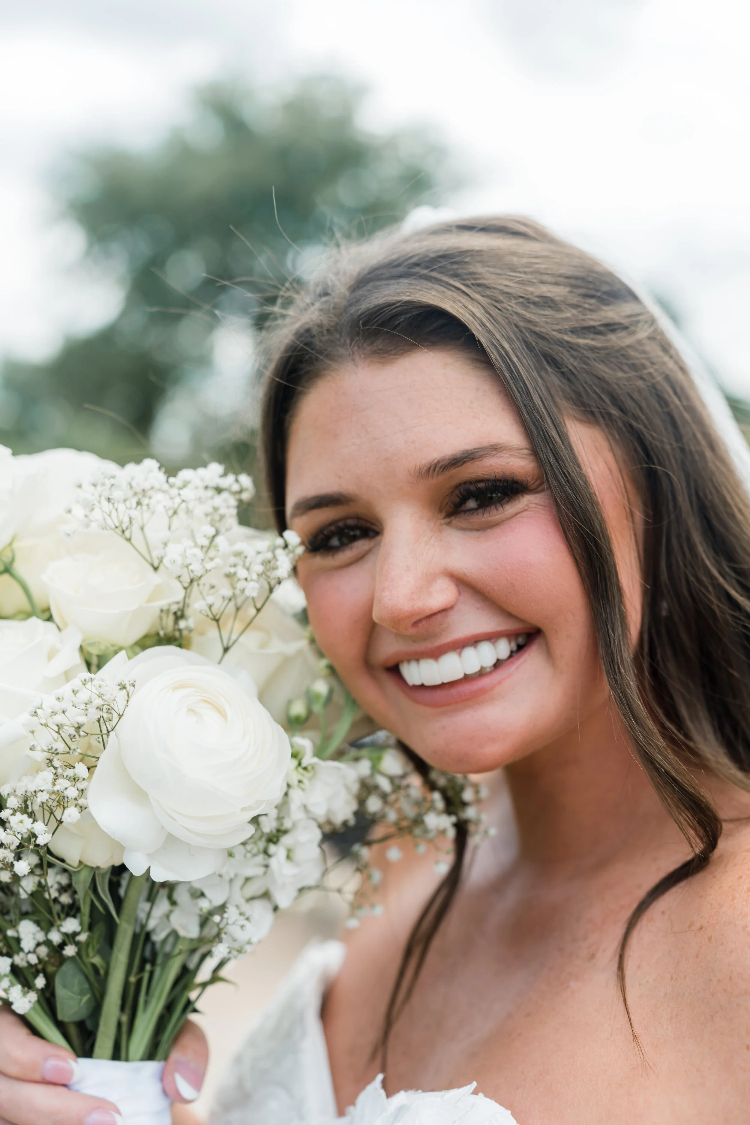 A woman with long brown hair smiling and holding a bouquet of white flowers.