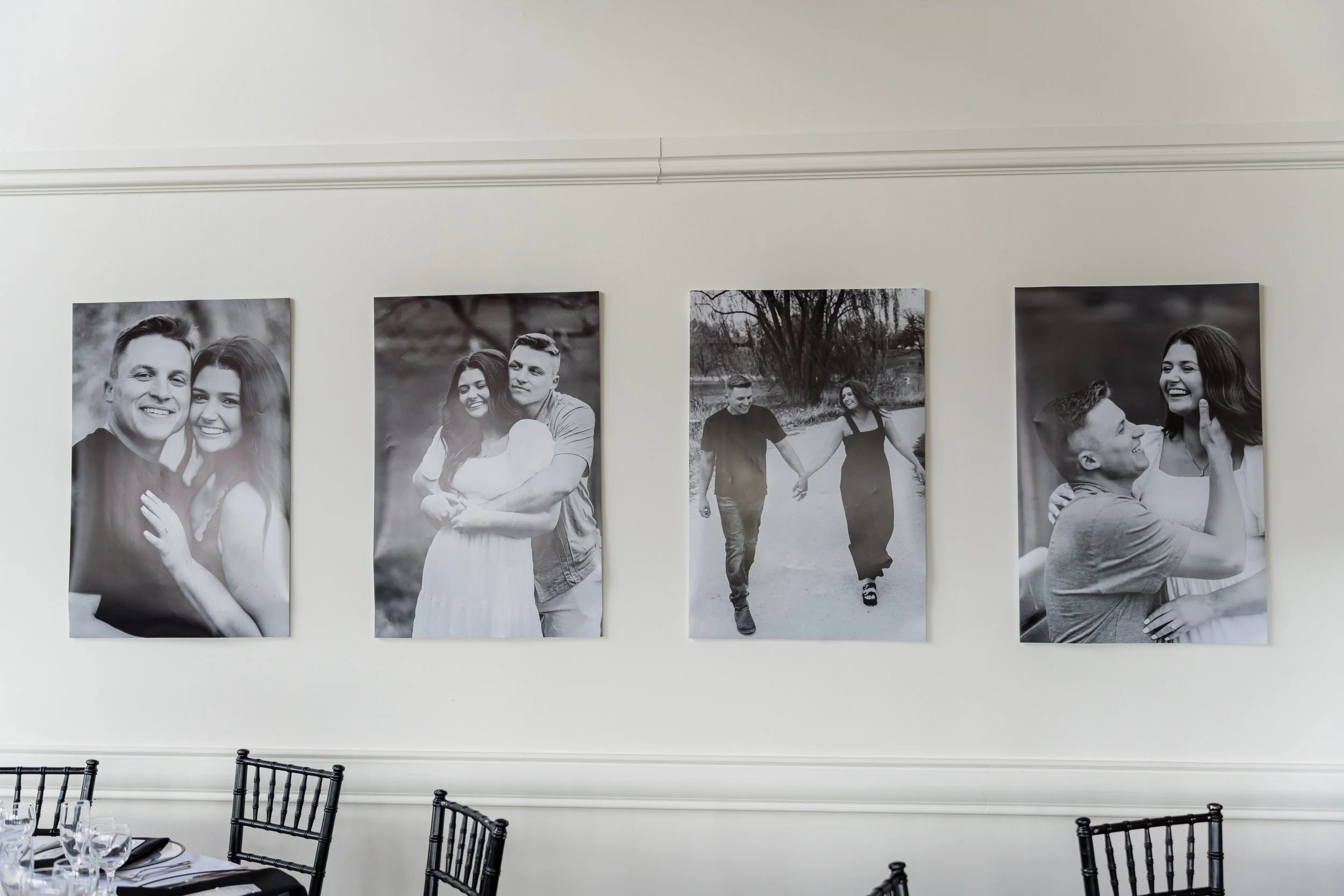 Four black-and-white photographs of couples hanging on a white wall, with a dining table and black chairs below.