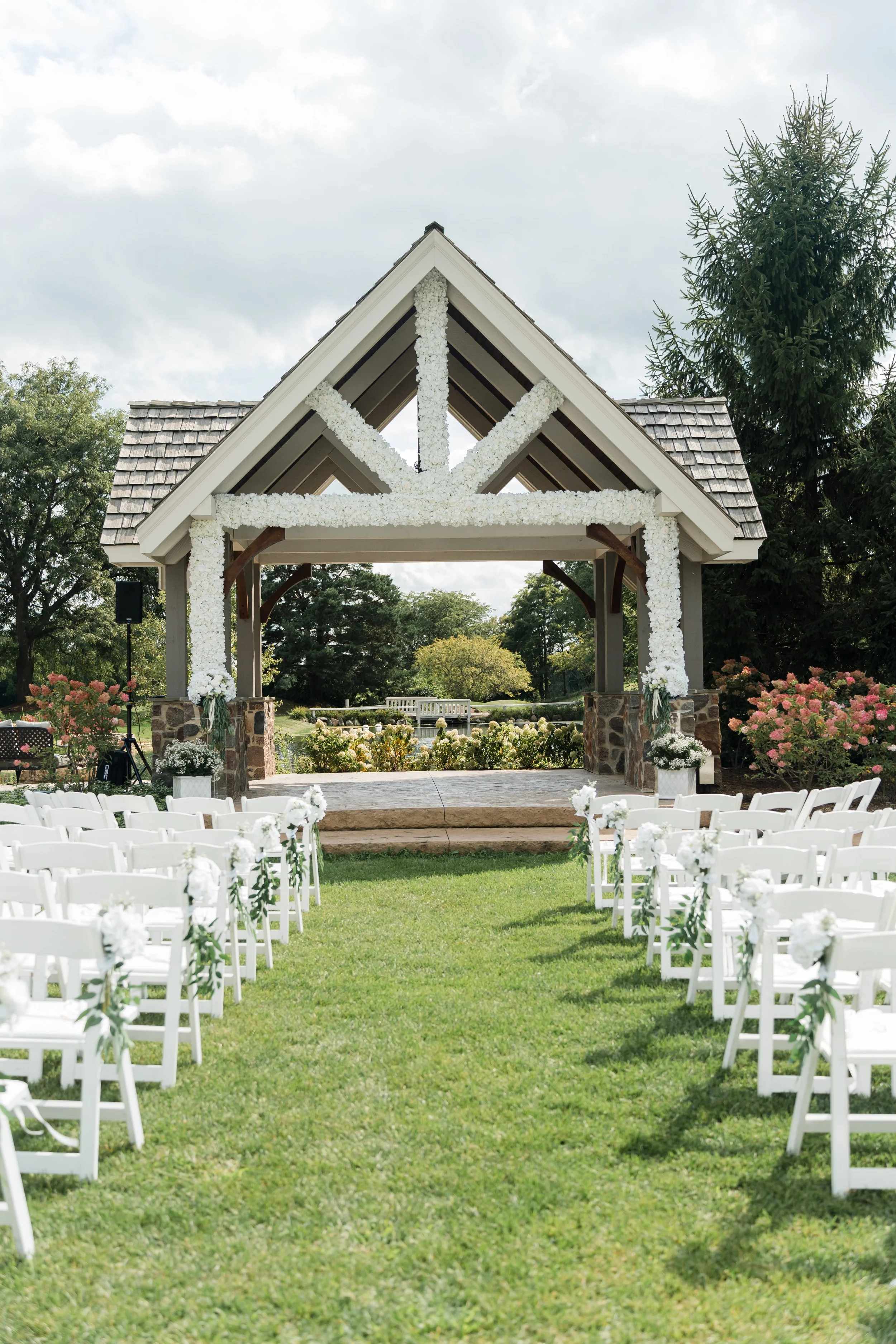 Outdoor wedding ceremony setup with white chairs and floral decorations under a decorated pavilion