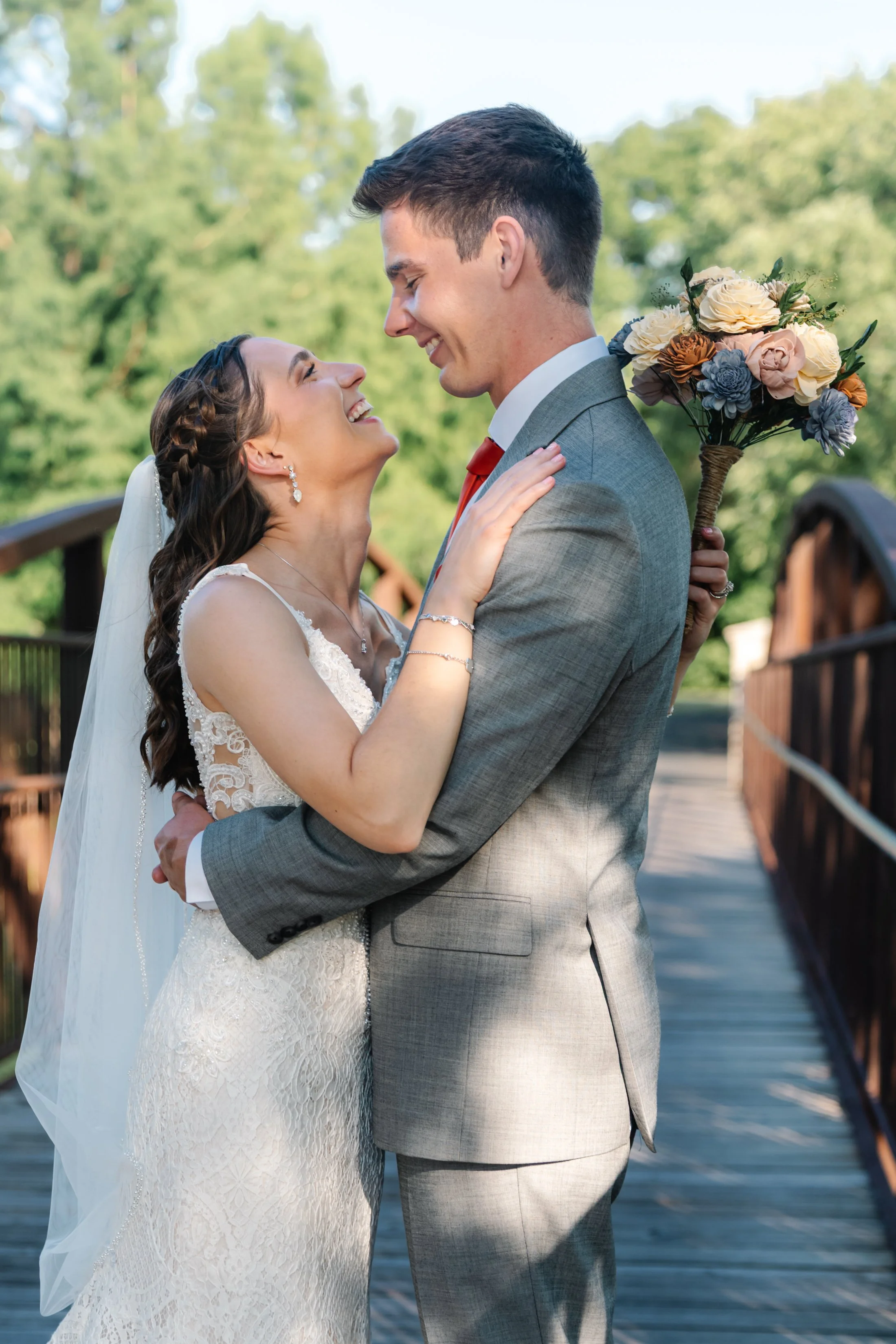 A bride and groom happily embracing outdoors on their wedding day, with the bride holding a bouquet of flowers.