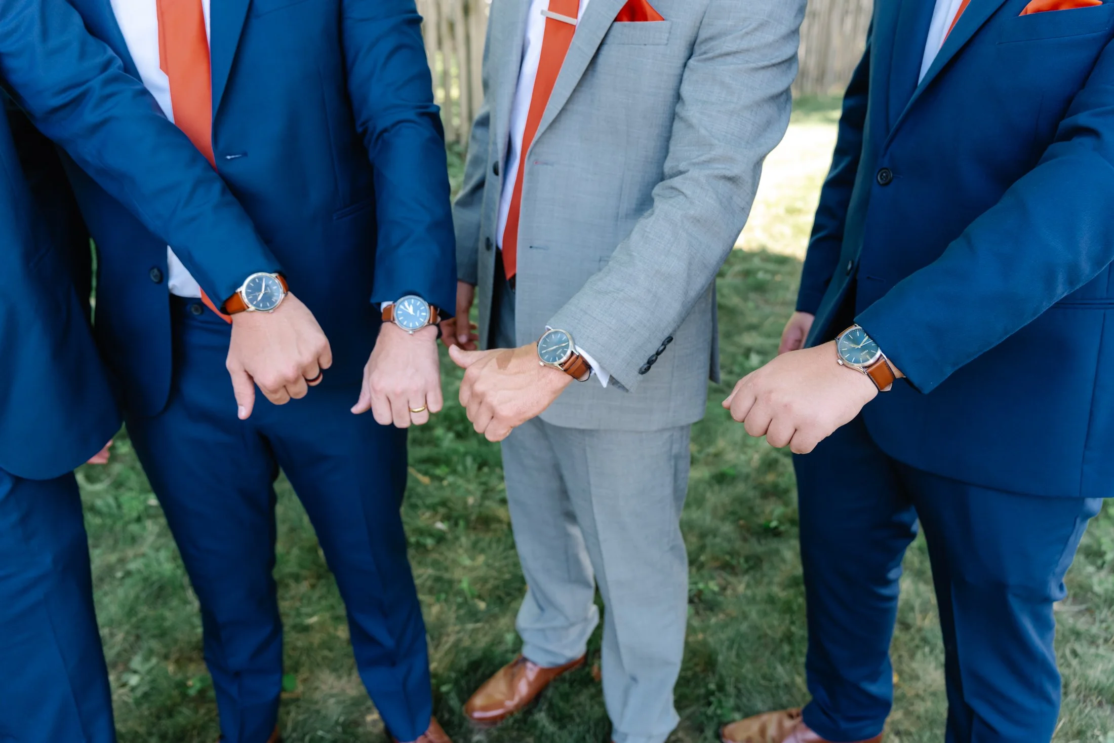 Group of men in suits showing off matching watches on their wrists, outdoors.