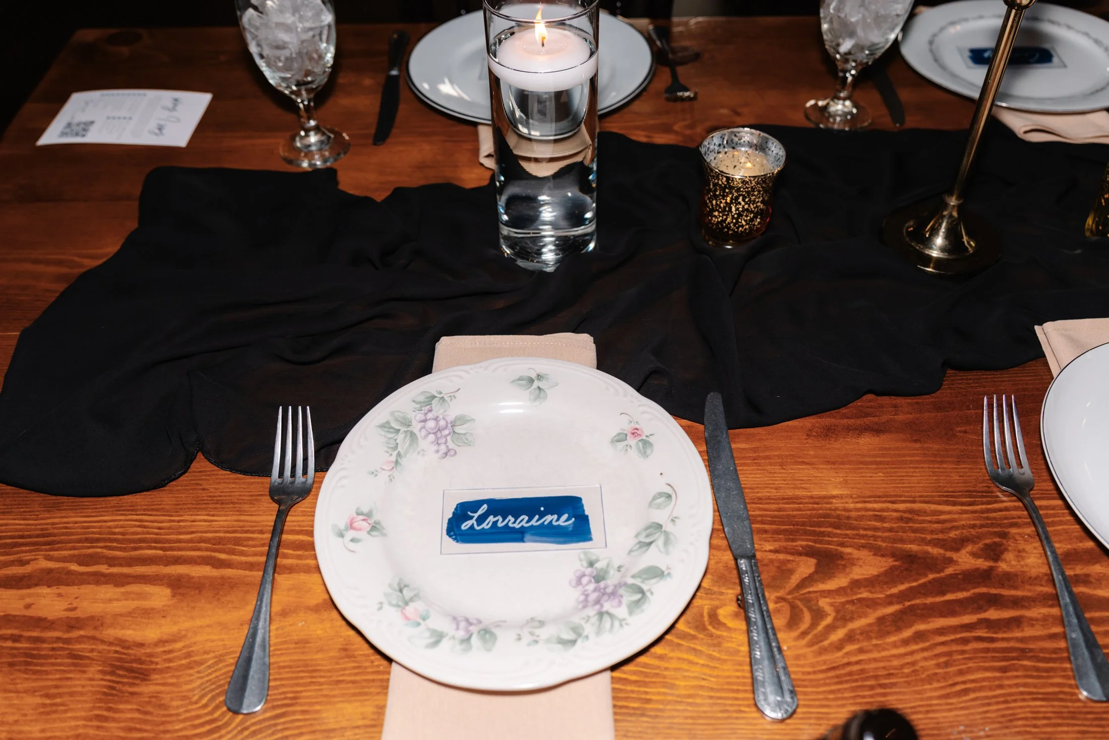Table setting with plates, silverware, glasses, and a black table runner, including a personalized place card that says "Lorraine."