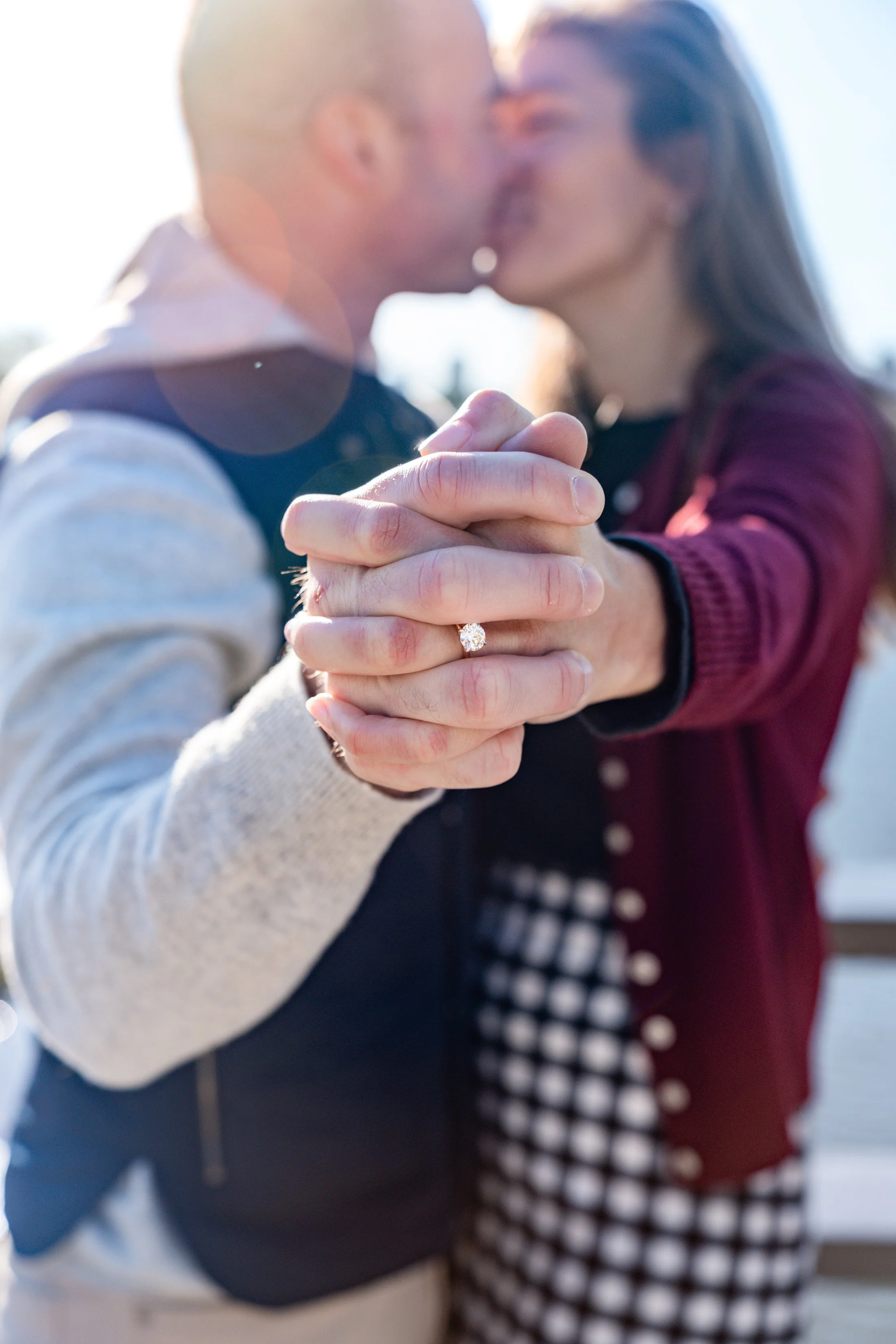 A couple kissing in the background, holding hands with an engagement ring visible on the woman's finger.