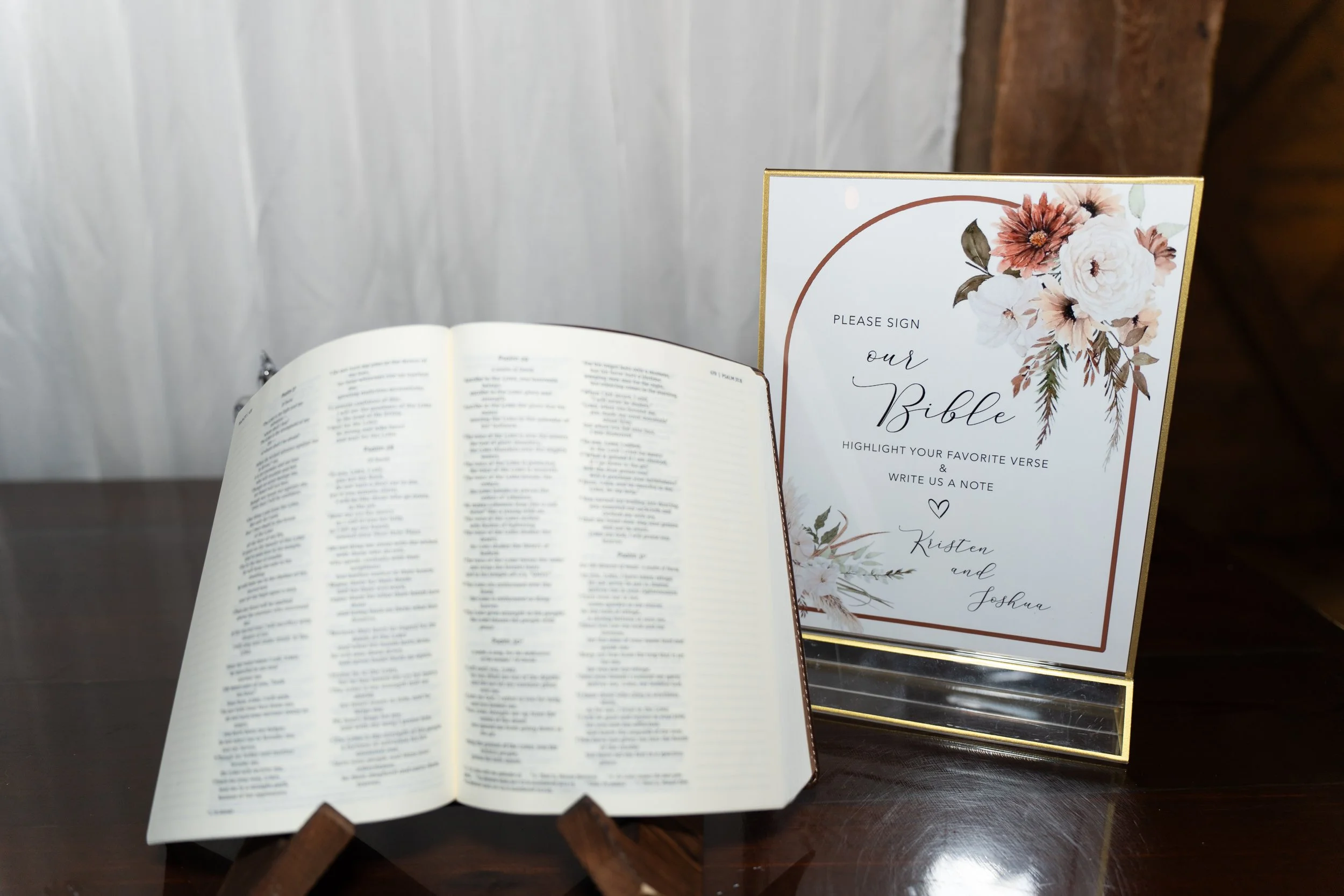 Open Bible placed on a stand and a sign that reads 'Please sign our Bible, highlight your favorite verse & write us a note, Kristen and Joshua' with floral design.
