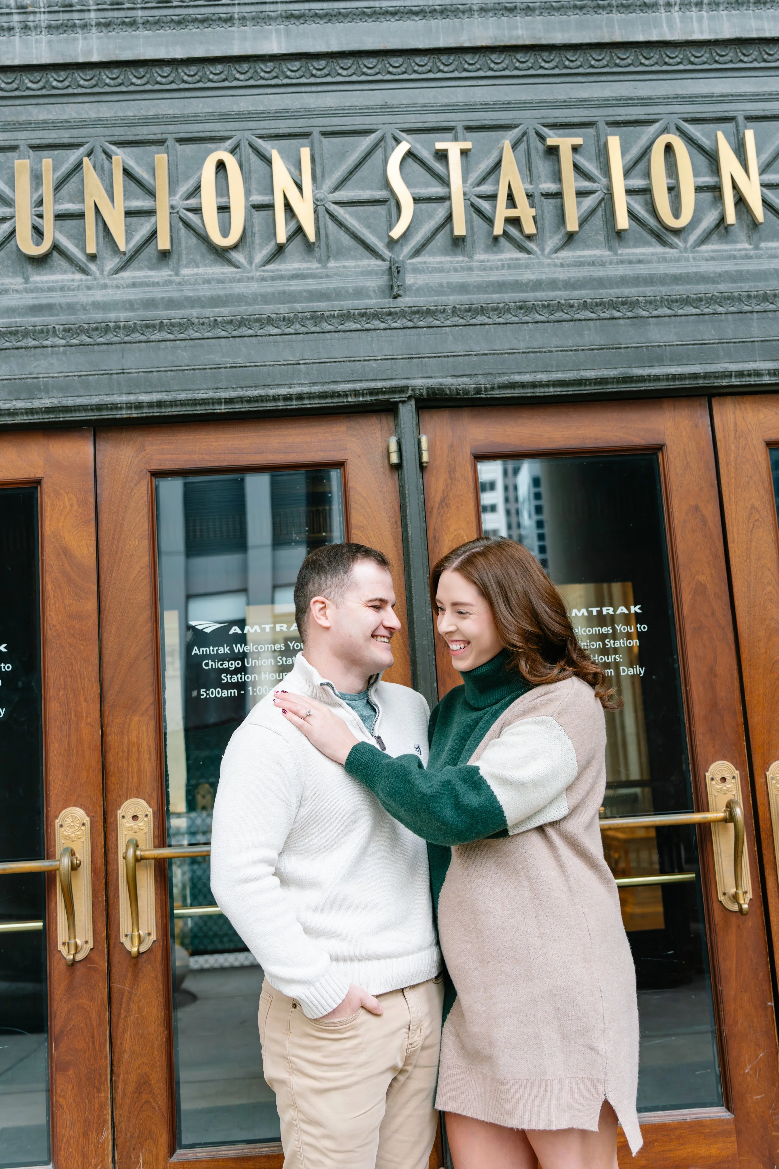 A smiling couple standing outside Chicago Union Station, with the station's sign above them and glass doors behind them.
