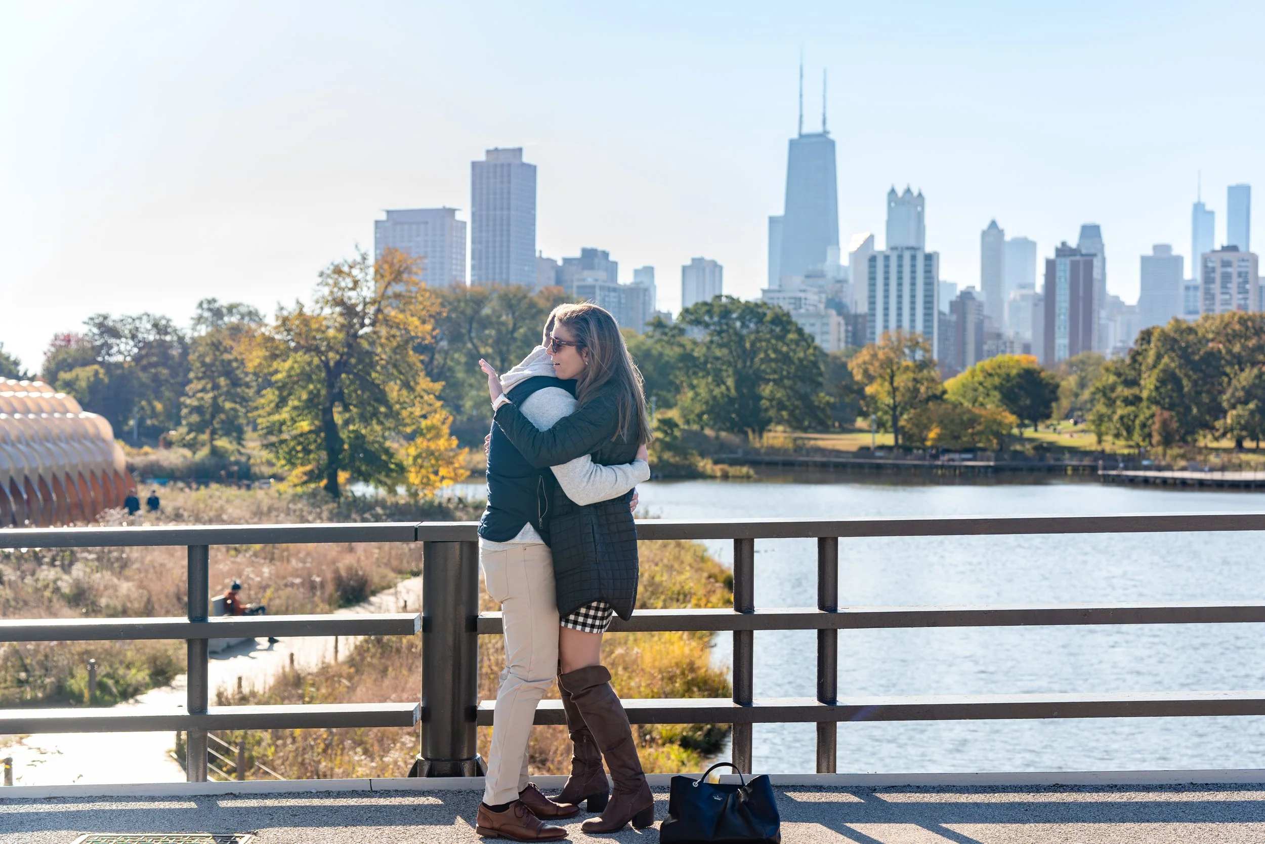 Two women hugging by a river with Chicago skyline in the background.