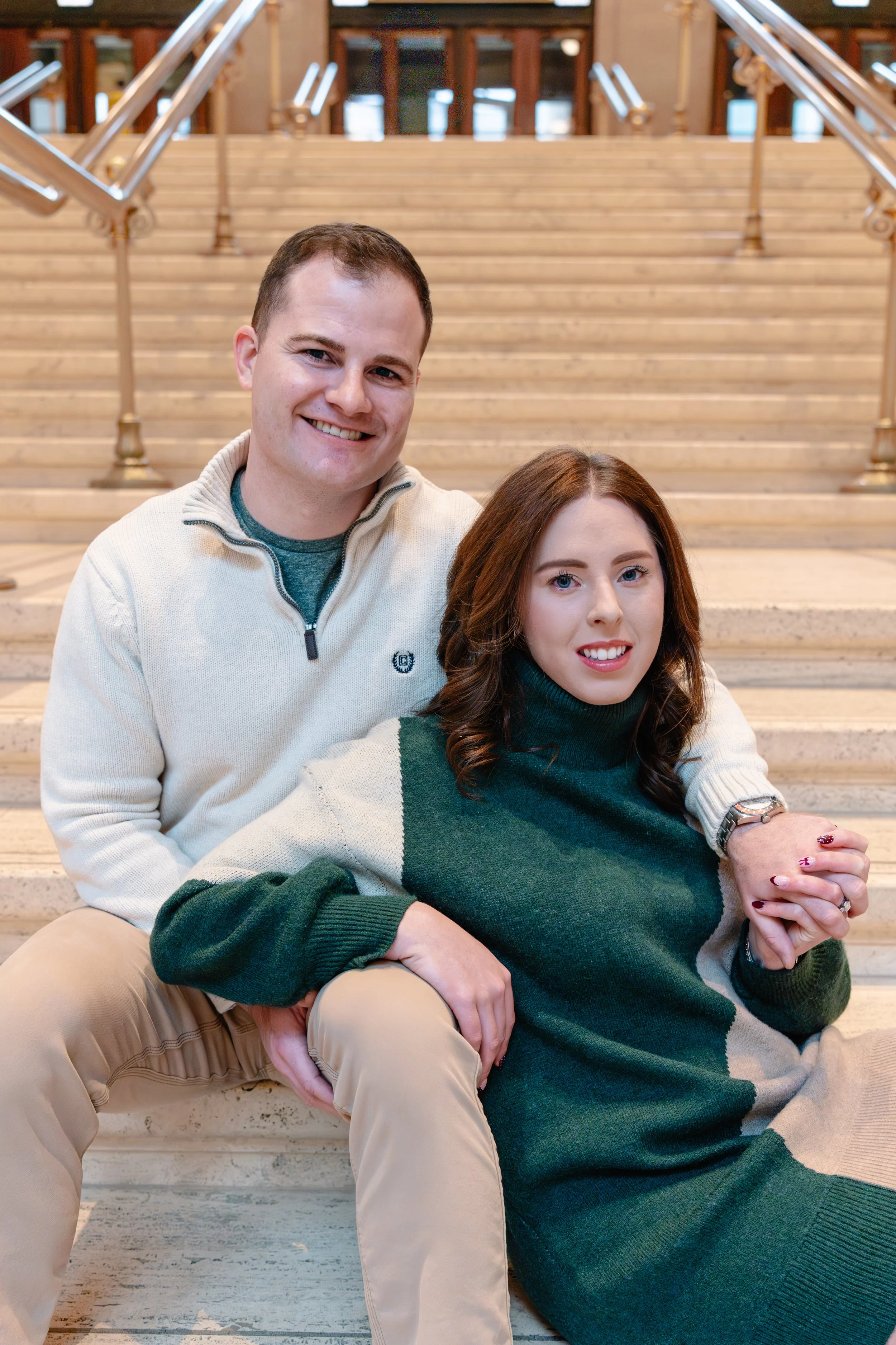 A smiling man sitting behind a woman on staircase in a building with wooden railings.