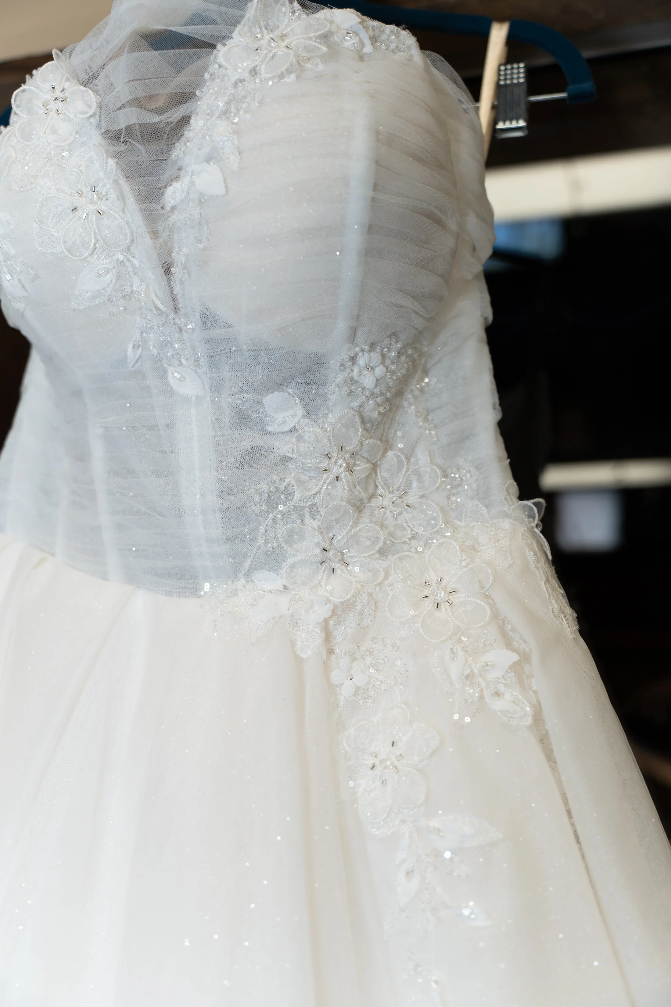 Close-up of a white wedding dress with lace and floral embroidery, hanging on a hanger.