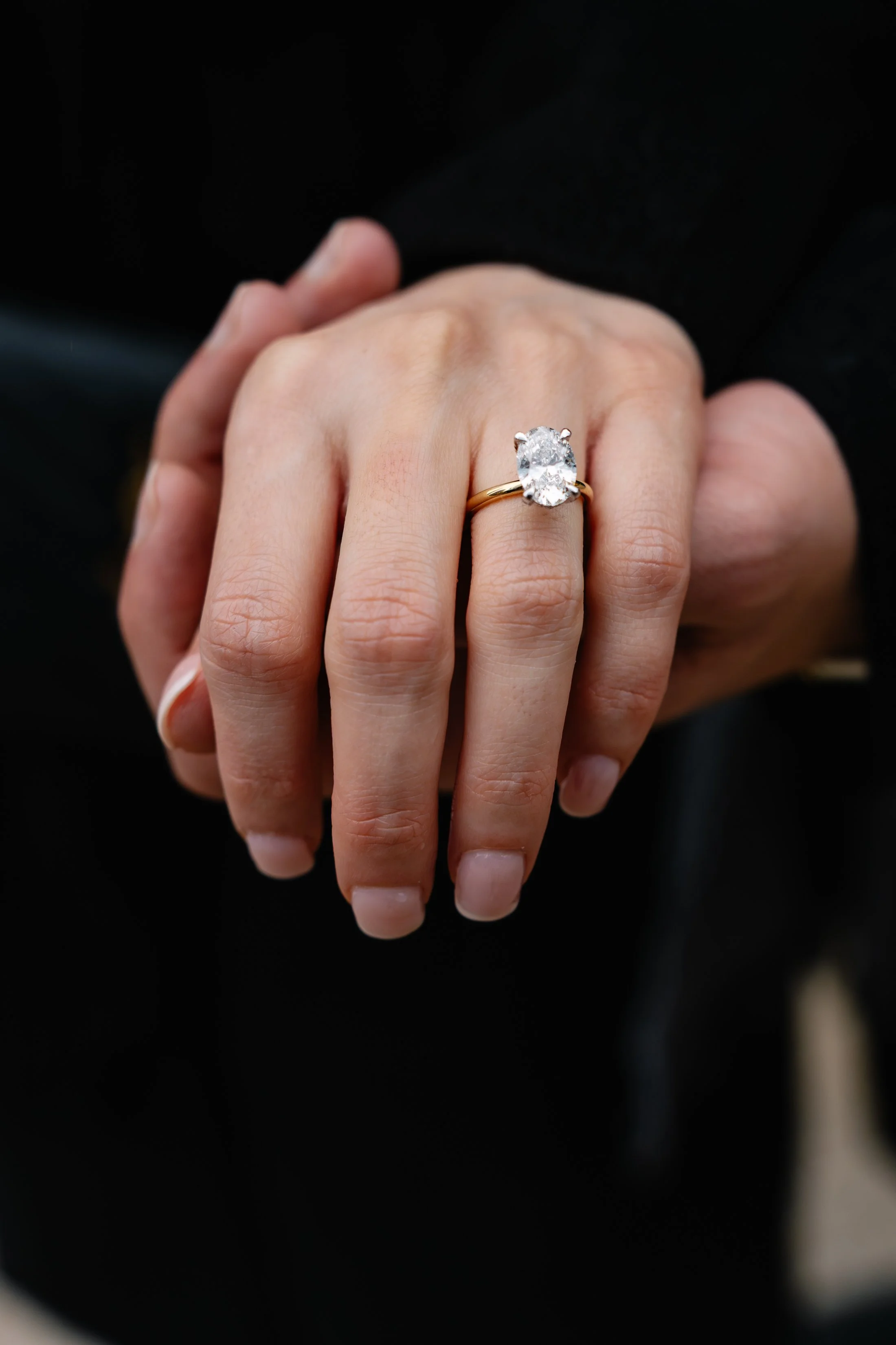 A hand with a large diamond engagement ring on the ring finger.