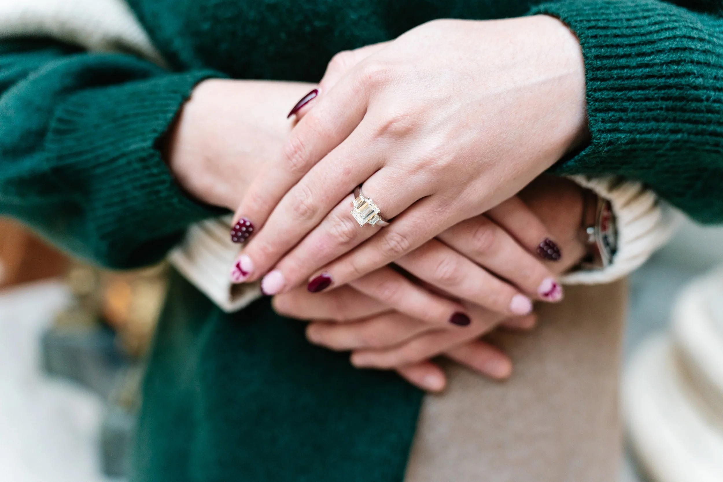 Hands with rings resting on a person's lap, wearing green and beige sweaters.