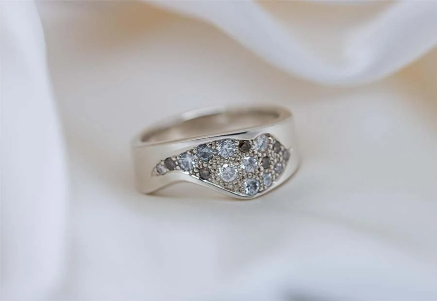 Silver ring with multiple small diamonds set on an elegant band, resting on a white fabric background.