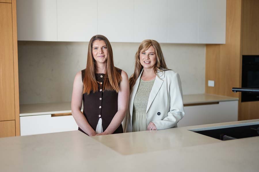 Two women standing in a modern kitchen, smiling at the camera.