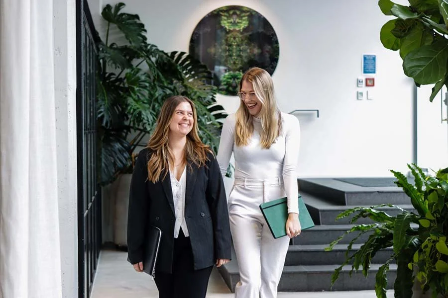 Two women walking and talking in a modern, green indoor space, smiling and laughing.
