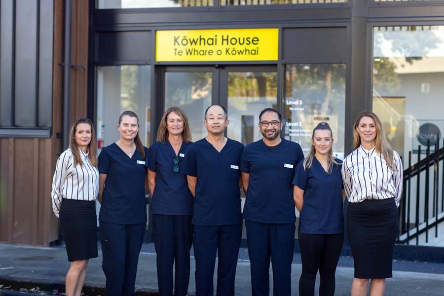 Group of six staff members standing outside Kuwhai House in front of the entrance, smiling for a photo.
