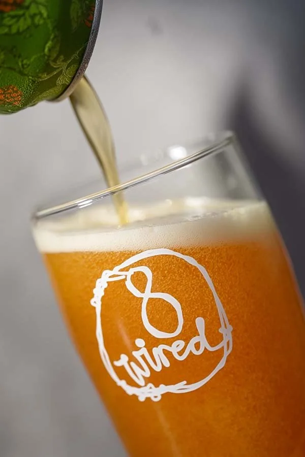 A glass of beer with the word "Tired" written on it, with beer being poured from a can above.