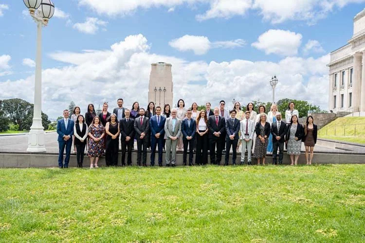 Group of people posed in front of a historic monument on a grassy area, under a partly cloudy sky.