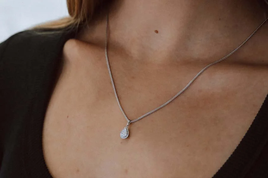 Close-up of a woman's neck wearing a silver chain necklace with a pear-shaped diamond pendant.