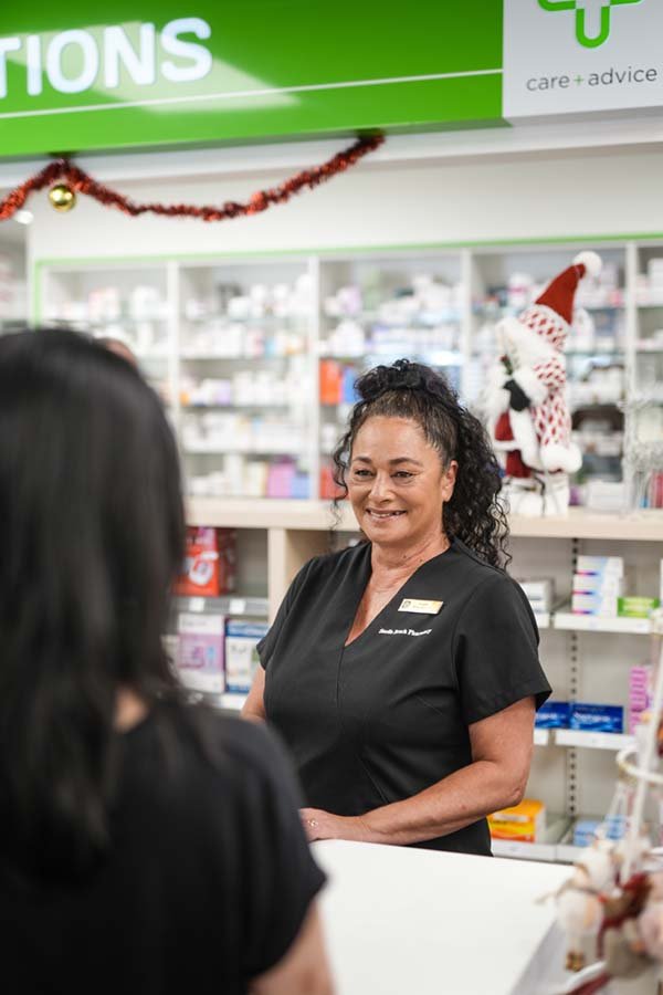 A female pharmacist smiling while assisting a customer at a pharmacy counter during the holiday season.