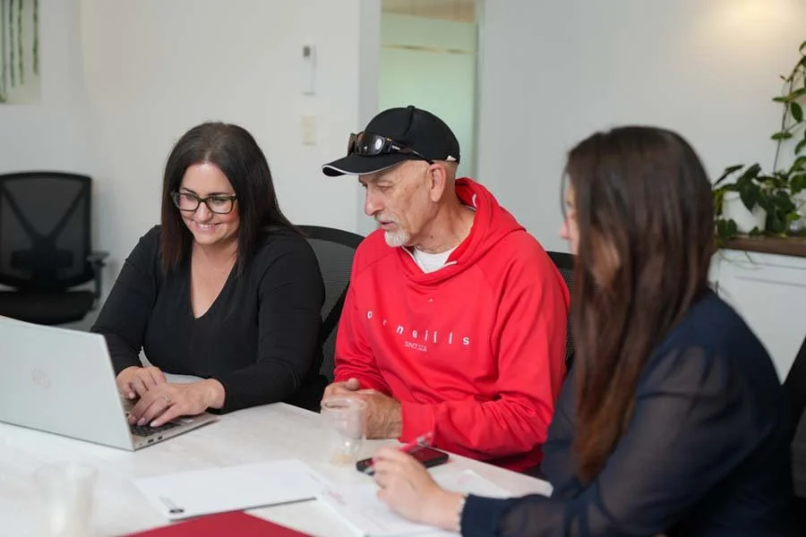Three people sitting at a table in an office, looking at a laptop and discussing.