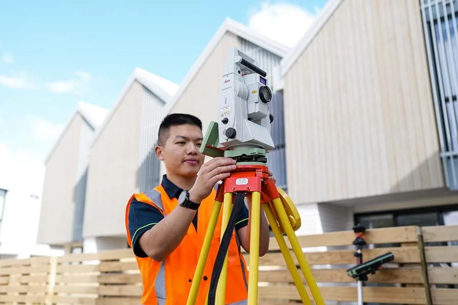 A surveyor using a total station instrument on a tripod at a construction site.