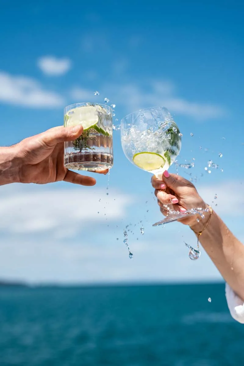 Two people toasting with glasses of water with lime and mint against a blue sky and ocean background.