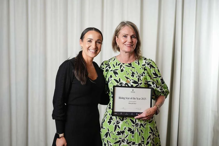 Two women smiling, standing in front of a white curtain. One woman holds a framed award titled 'Rising Star of the Year 2025' for Body & Soul.